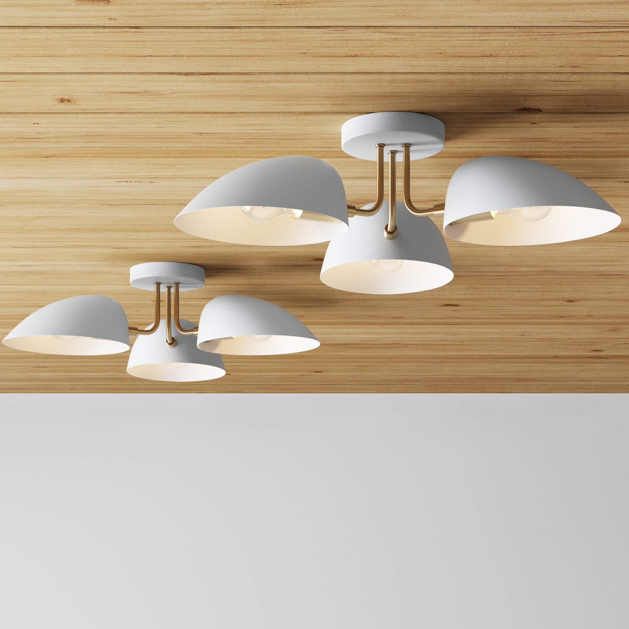 Two sets of Nathan James Metal 3-Arm Flush Mount Ceiling Lights in white are mounted on a light wooden ceiling above a white wall, featuring dome-shaped shades and gold accents for a minimalist, mid-century modern style.