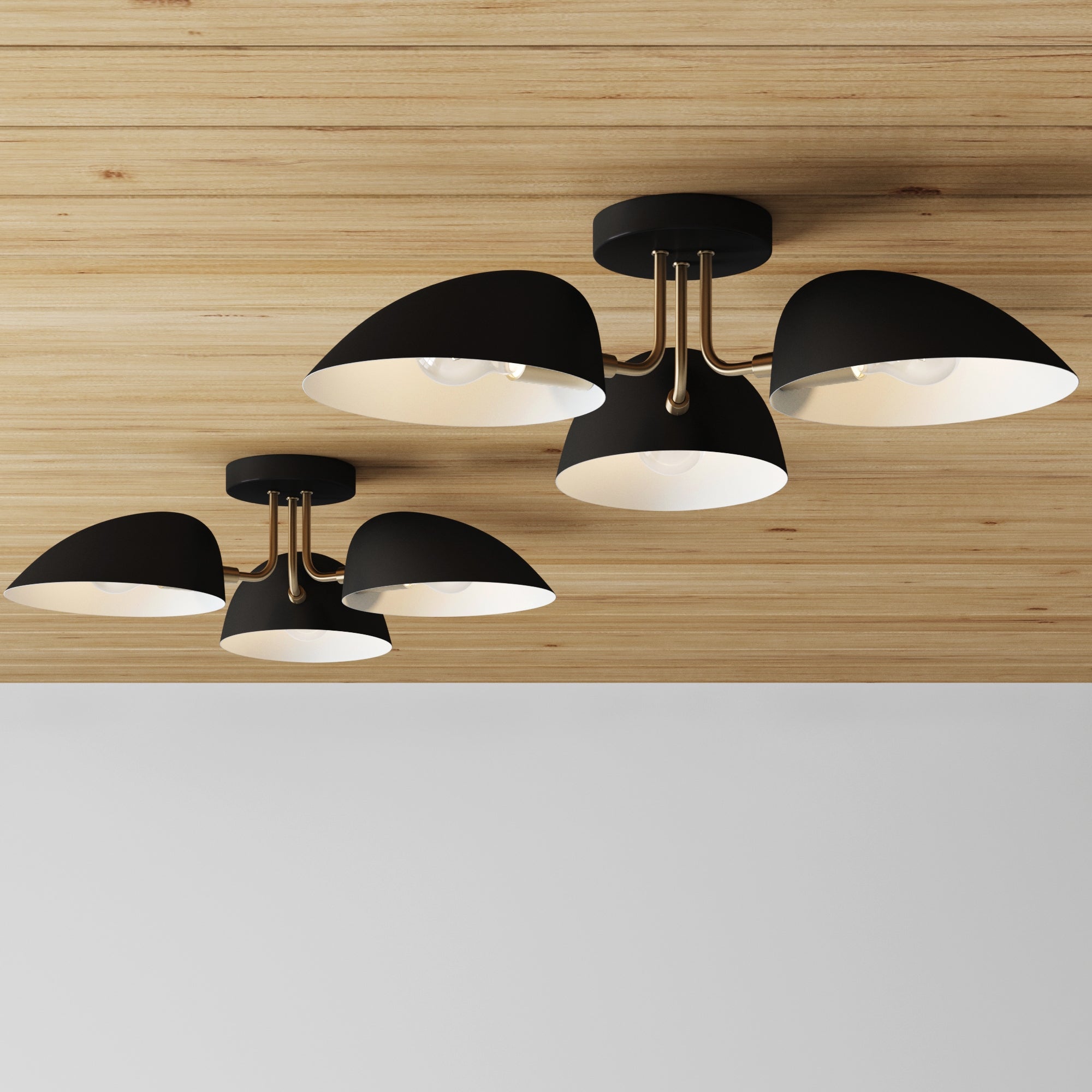 Two sets of Nathan James Metal 3-Arm Flush Mount Ceiling Lights in black are installed on a wood ceiling above a white wall, offering a sleek, minimalist look inspired by mid-century modern design.