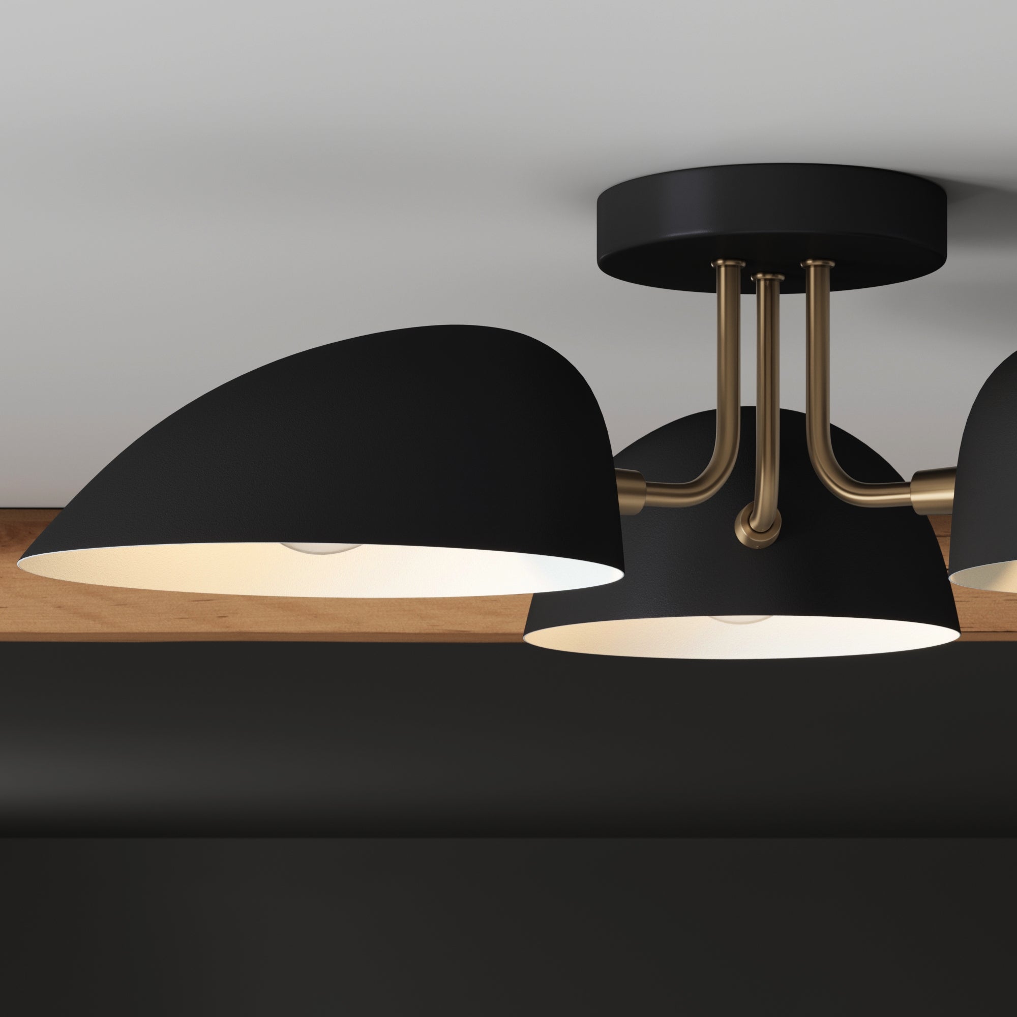 Modern ceiling light fixture with two black, dome-shaped shades and brass arms, mounted on a black circular base against a white ceiling and a wooden accent.