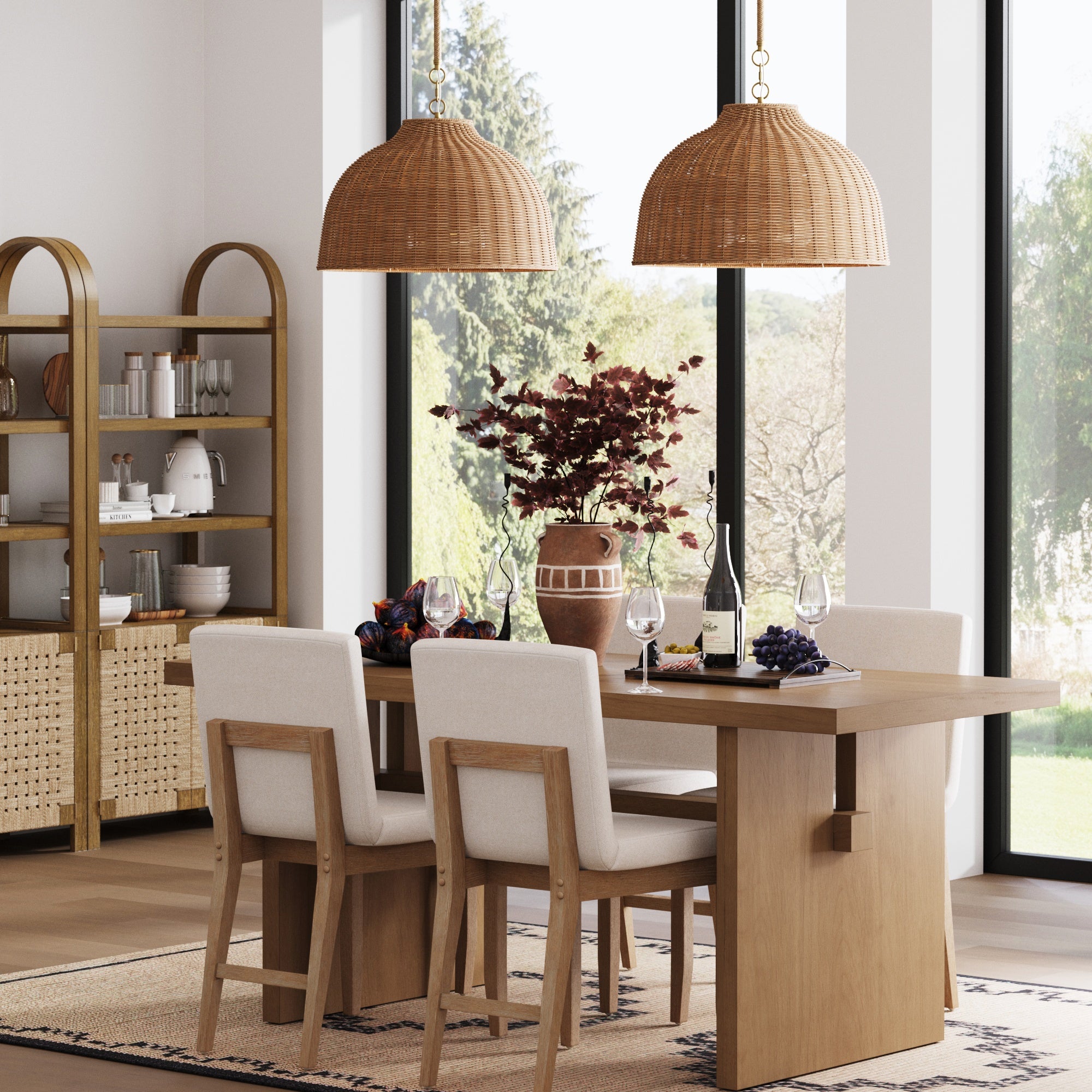 Modern dining room with a light wood table, six upholstered chairs, large windows, and two Nathan James Modern Farmhouse Rattan Dome Pendant Lights. Table set with glassware, wine, red foliage vase; shelf with dishes and decor in background.