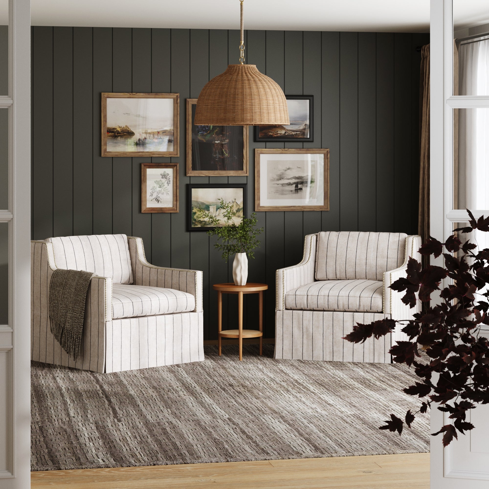 A cozy sitting area includes two striped armchairs, a small round table with a vase, and framed art on dark paneled walls. Overhead hangs the Nathan James Modern Farmhouse Rattan Dome Pendant Light. A gray rug covers the floor.