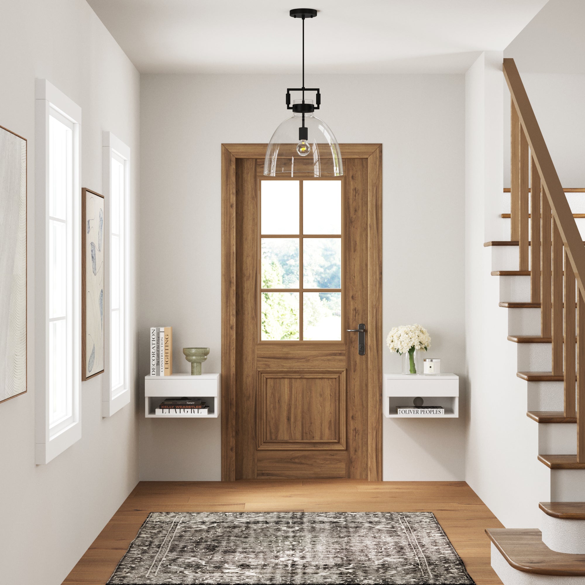 A bright entryway with a wooden front door, white walls, two floating shelves with books and decor, a black and white patterned rug, and a staircase with wooden railing on the right. A pendant light hangs from the ceiling.