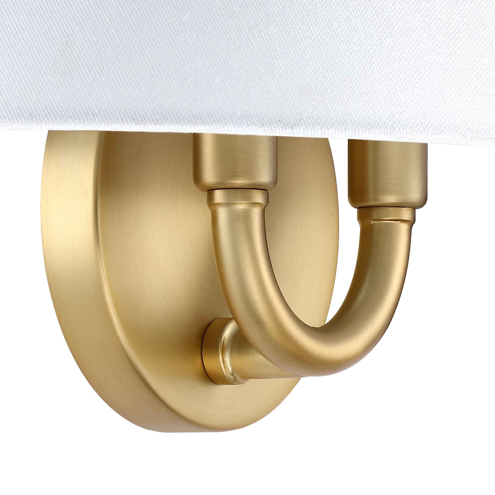 Close-up of a wall-mounted light fixture with a matte gold finish, featuring a curved arm extending from a round base and partially covered by a white lampshade at the top.