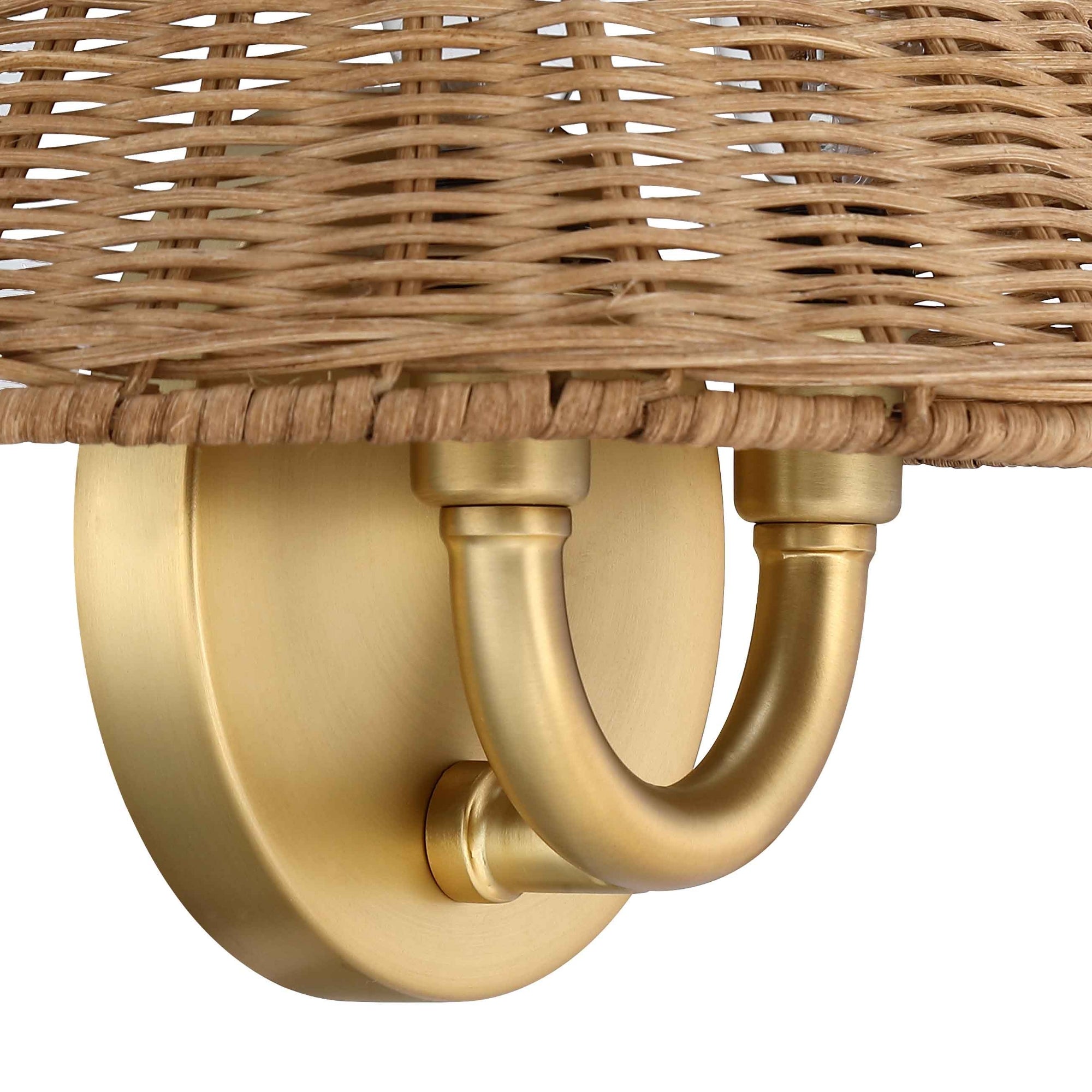 Close-up of a decorative wall sconce featuring a round brass base, two curved brass arms, and a woven rattan shade with a natural finish. The fixture combines modern and rustic design elements.