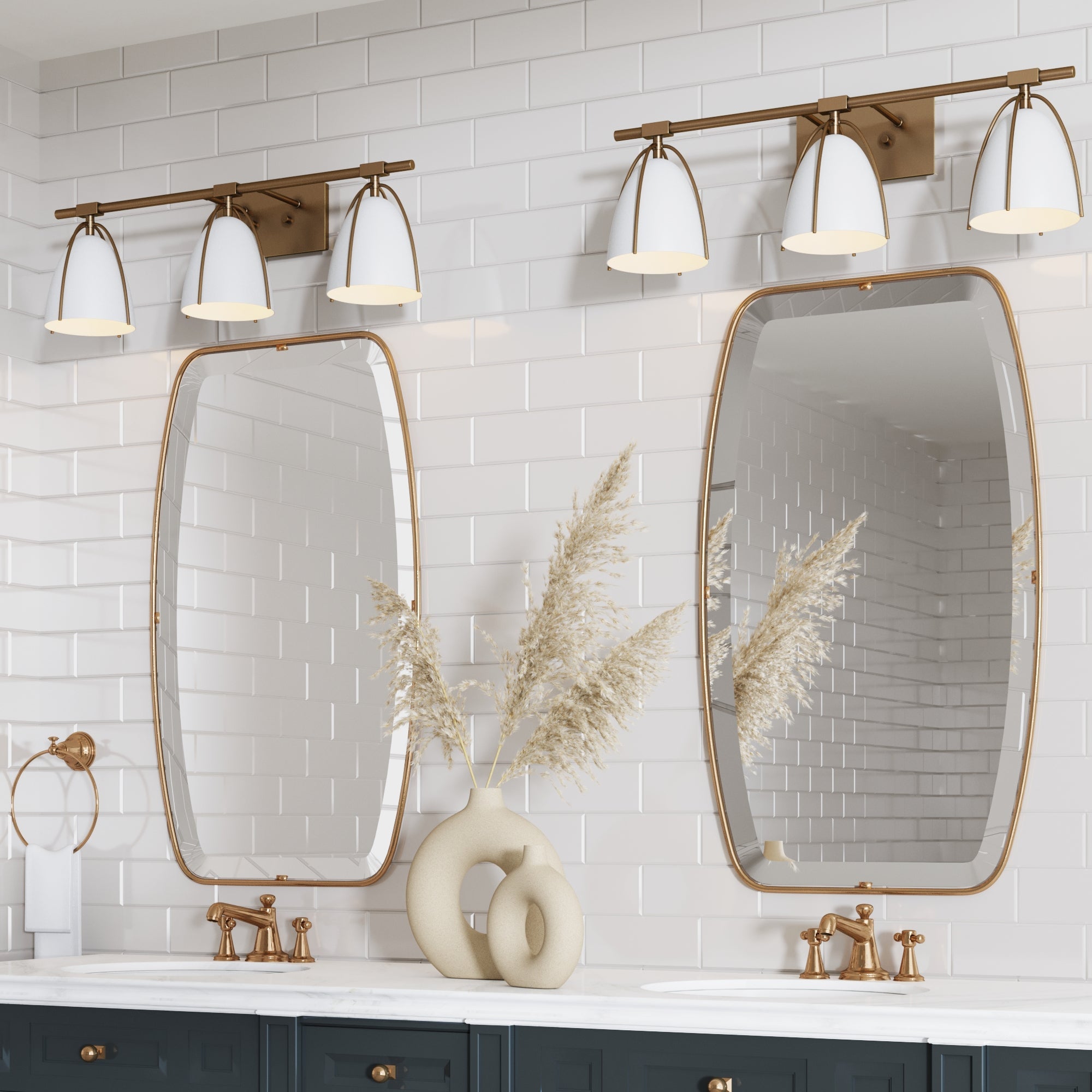 A modern bathroom includes two oval mirrors with gold frames, double gold faucets, white subway tile walls, and Nathan James Metal Cage Bathroom Vanity Lights (Set of 2). A sculptural vase with pampas grass sits on the marble countertop.
