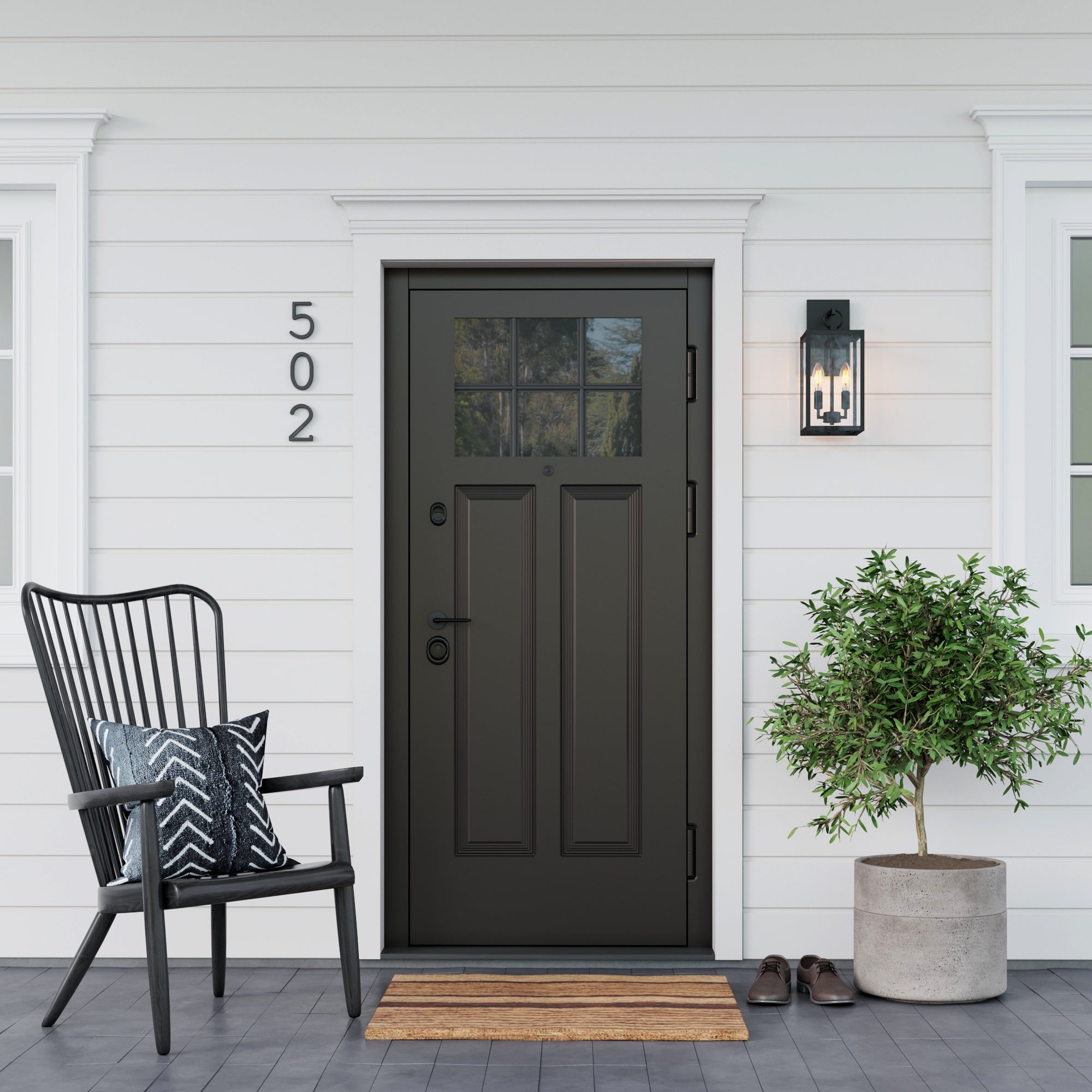 A black front door with glass panes is centered on a white house exterior. To the left is a black chair with a patterned pillow, and to the right is a potted plant and a pair of shoes. A wall lantern and house number 502 are visible.