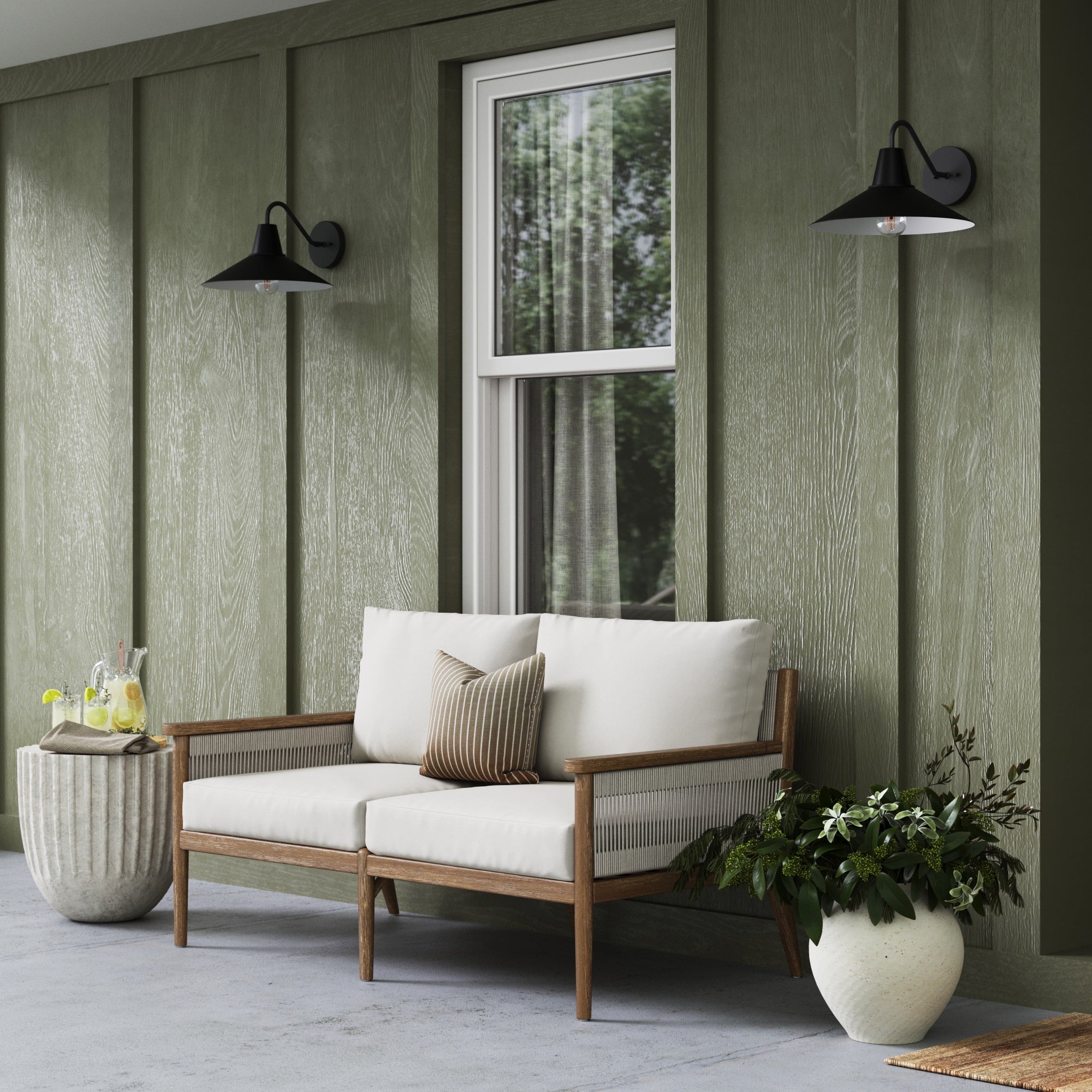 A cozy outdoor patio features a wooden loveseat with cream cushions, a striped pillow, potted plants, and stylish indoor-outdoor lighting from the Nathan James Indoor or Outdoor Metal Decorative Wall Light (Set of 2) on green siding.