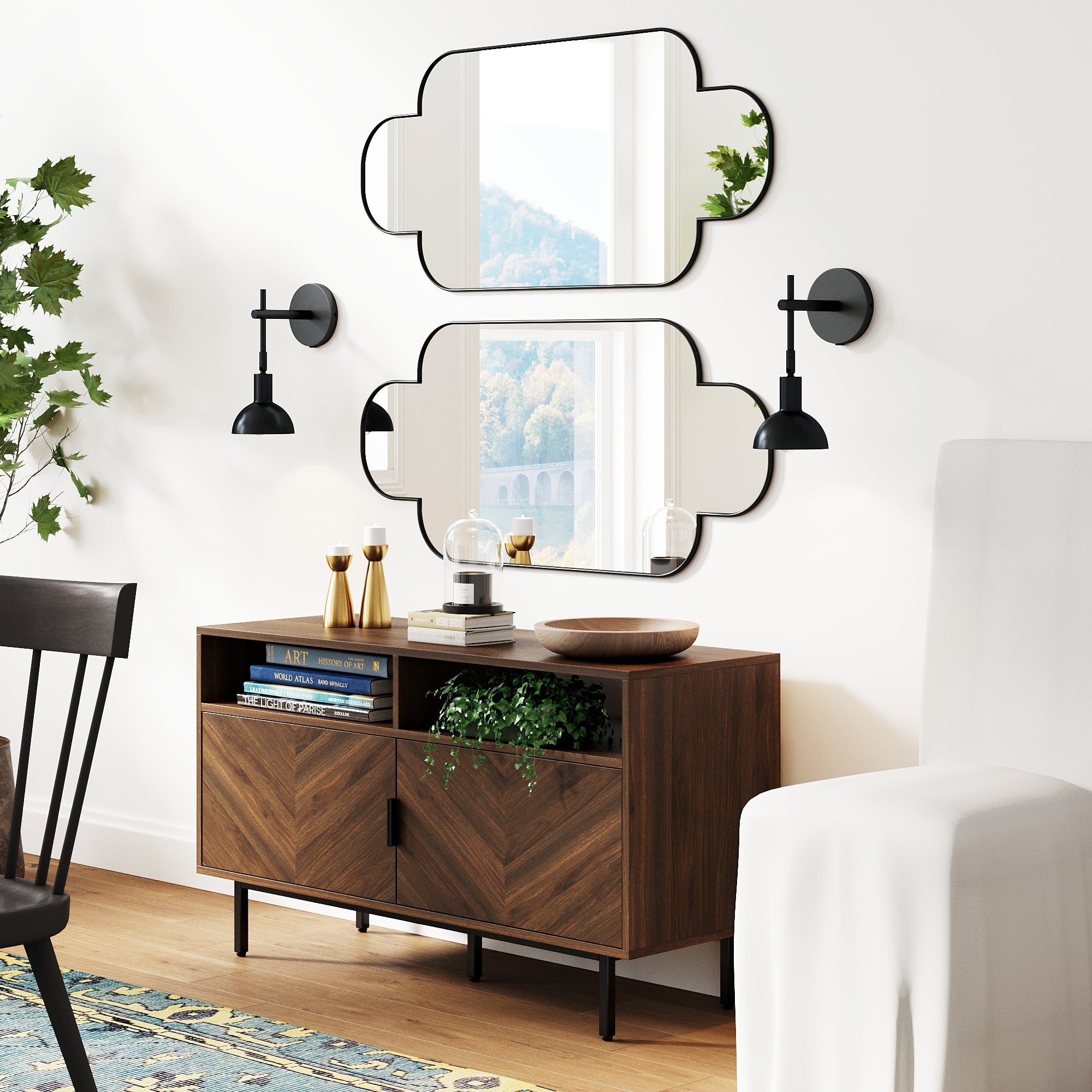 A modern living room features a wooden sideboard with chevron-patterned doors, decor, books, plants, two geometric mirrors above, and a pair of Nathan James Plug-in Metal Wall Lights Black on either side; a chair and rug are partially visible.