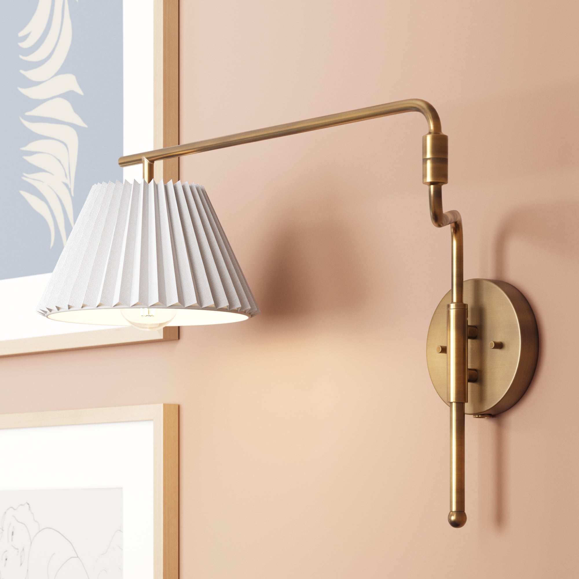 Brass wall-mounted lamp with an adjustable arm and pleated white lampshade, installed on a peach-colored wall above framed artwork.