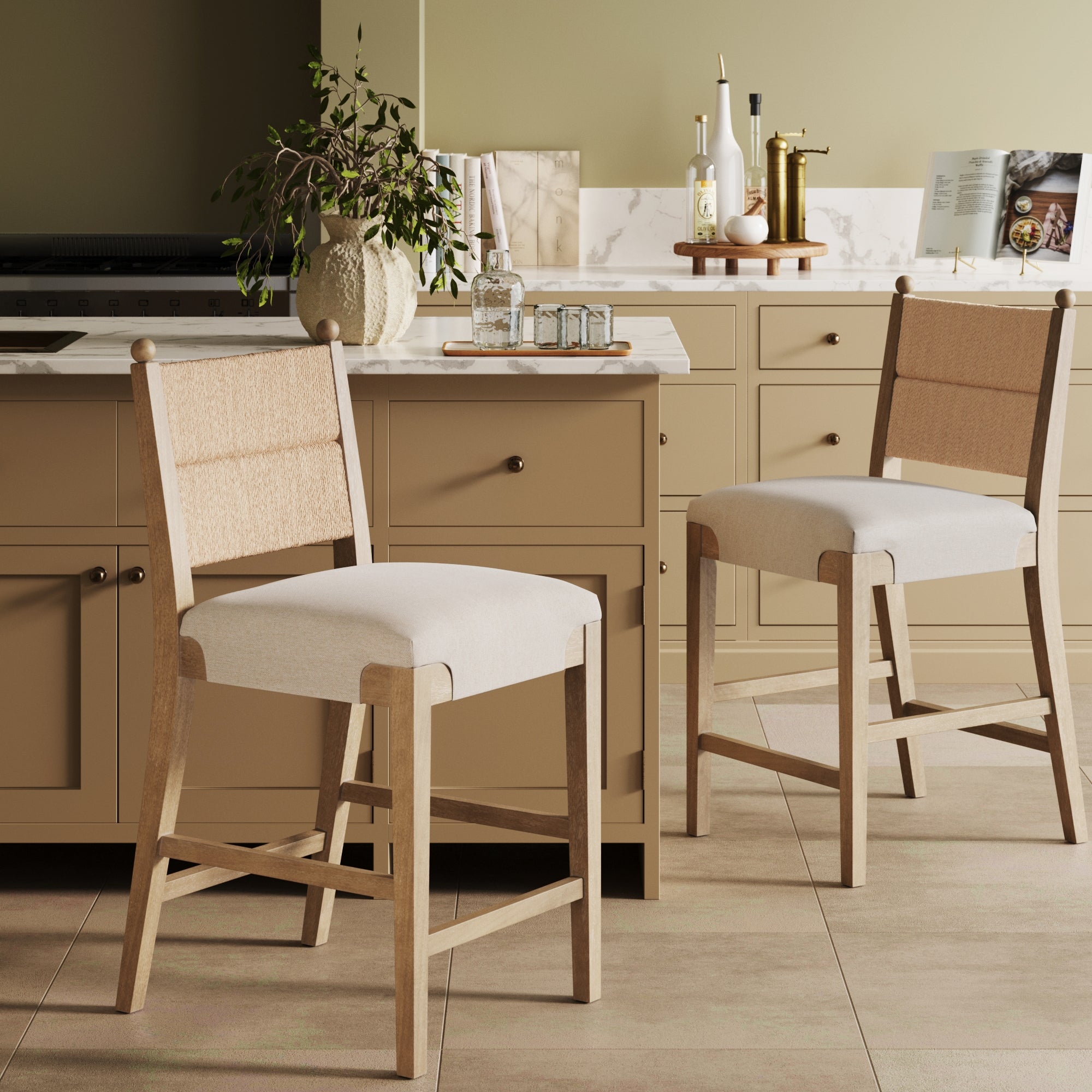 Two Seagrass & Wood Counter Height Bar Stools (Set of 2) by Nathan James in light brown are set at a beige kitchen island. The cozy, modern space features beige cabinets, a plant, and various kitchen essentials.