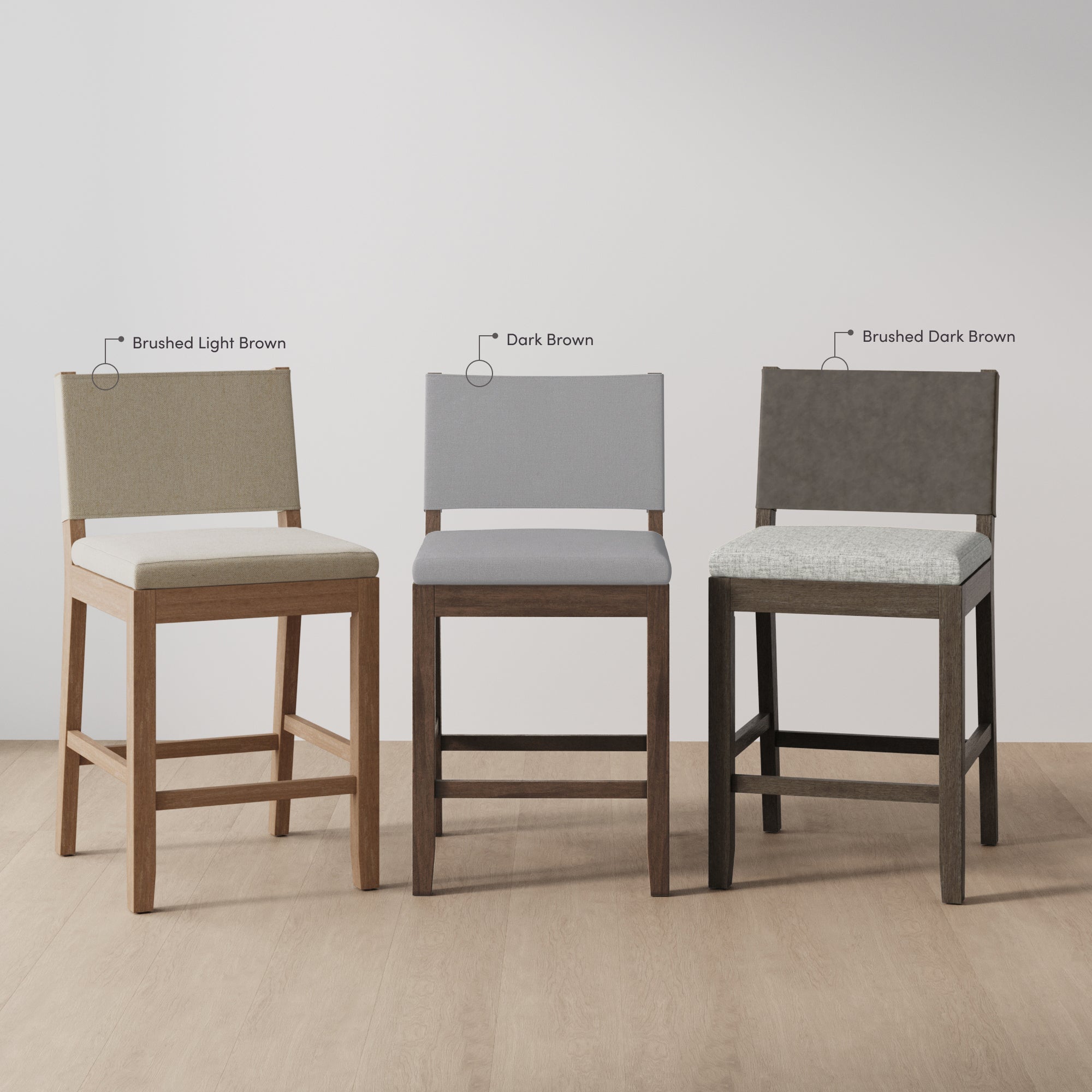 Three upholstered bar stools with wooden legs are shown side by side on a light wood floor. From left to right, the fabric colors are labeled Brushed Light Brown, Dark Brown, and Brushed Dark Brown.