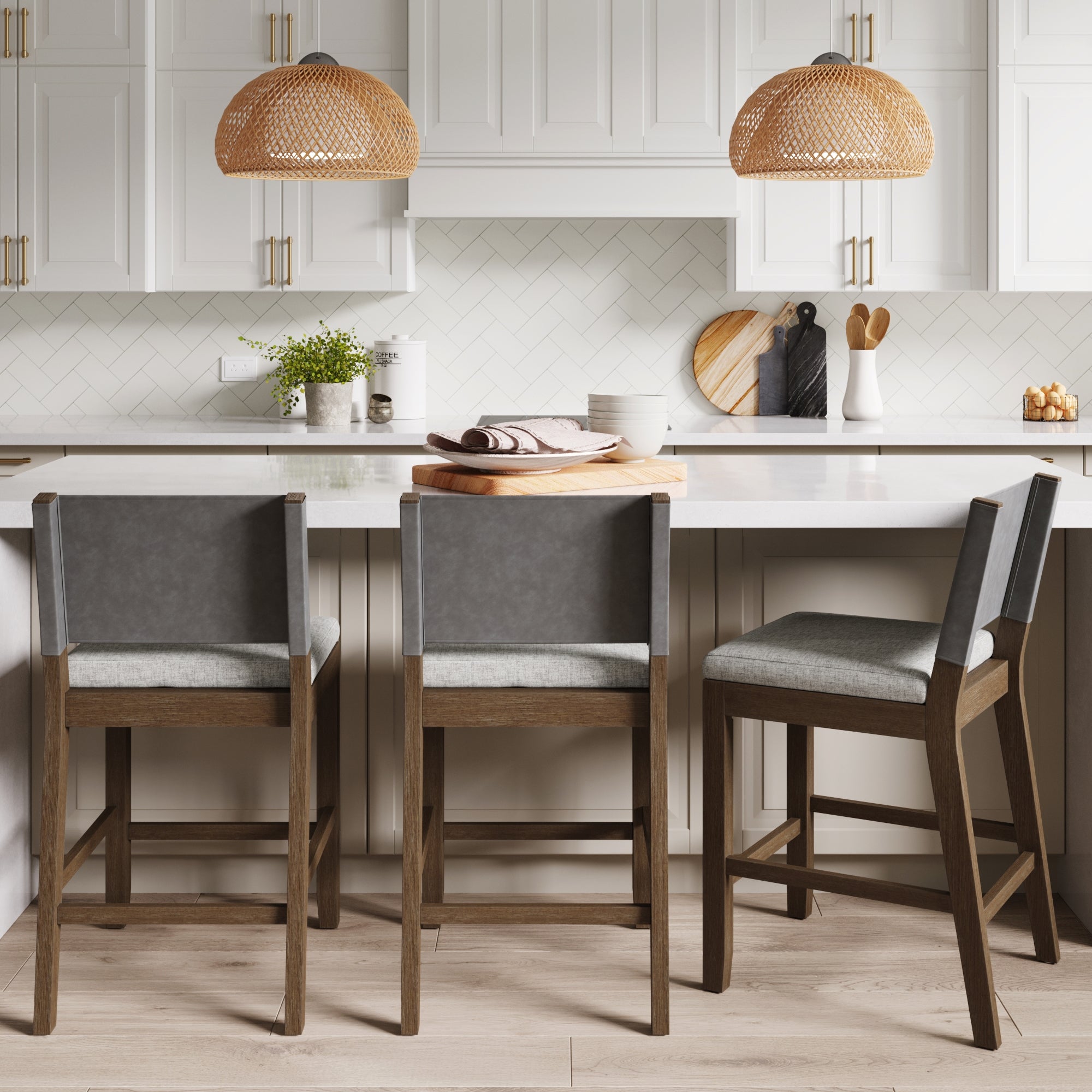 A modern kitchen with white cabinets, a white island with three gray and wooden bar stools, hanging wicker pendant lights, cutting boards, plants, and kitchen utensils on the countertop.