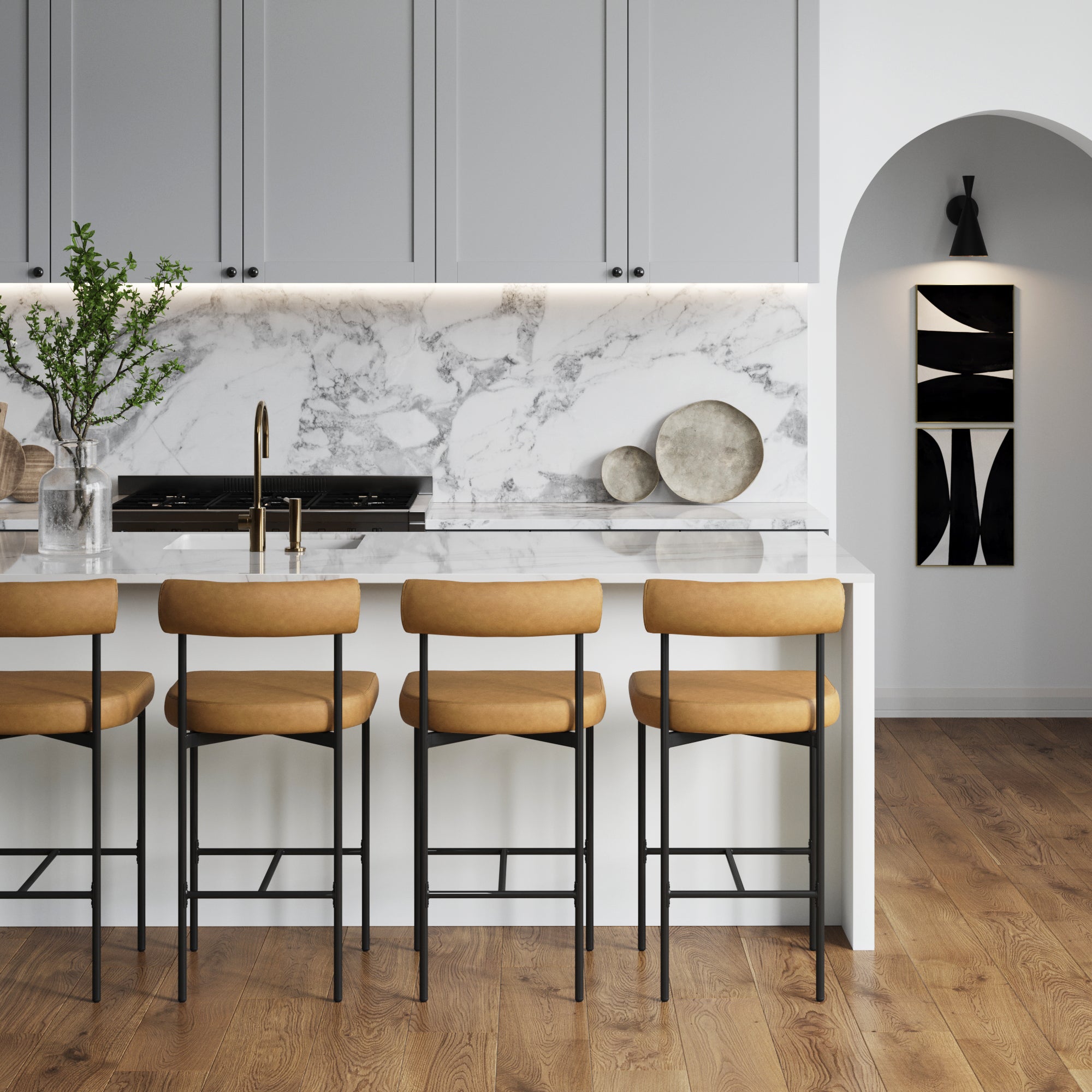Modern kitchen with light gray cabinets, marble backsplash, and white island lined with a set of 4 Nathan James Faux Leather Counter Height Bar Stools in brown. Wooden cutting boards, a vase with greenery, wood flooring, and an archway complete the look.