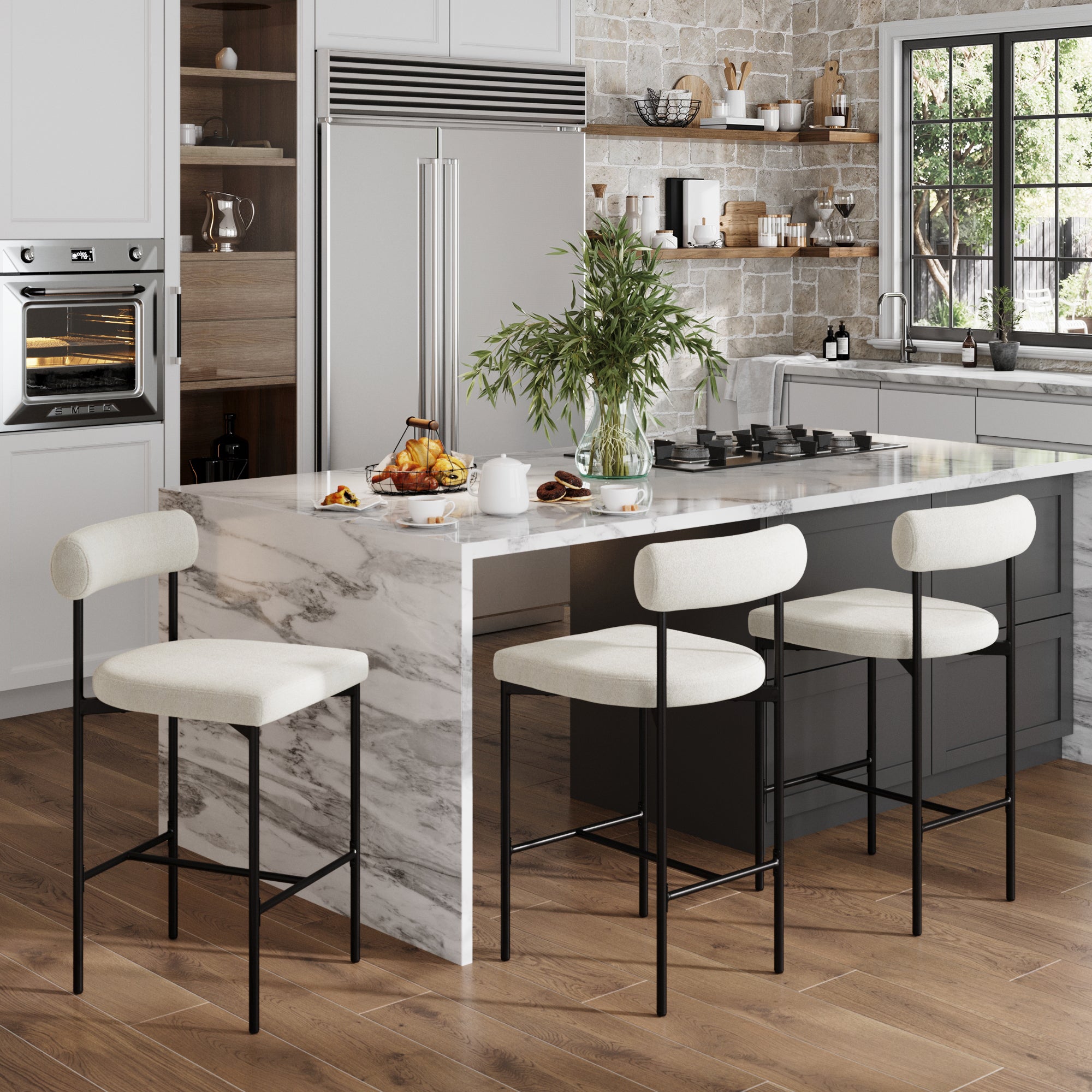 Modern kitchen with a marble island, wood floors, built-in appliances, large window with greenery view, and a vase of leafy branches. The island is lined with Nathan James Boucle Counter Height Bar Stools (Set of 3) in white with black legs.