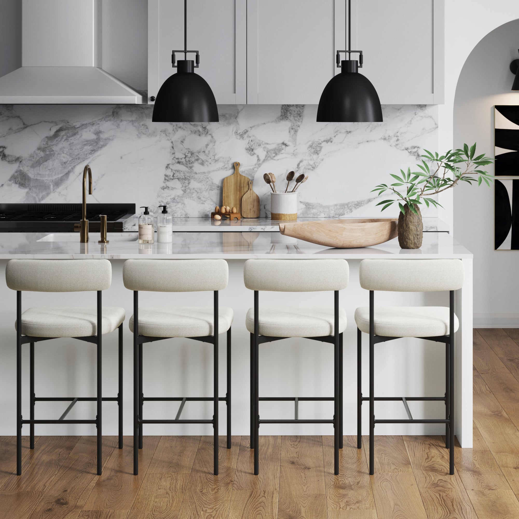 Modern kitchen with marble backsplash, white cabinets, gold faucet, and a white island with four cushioned bar stools. Two black pendant lights hang above the island, and a potted plant sits on the counter.