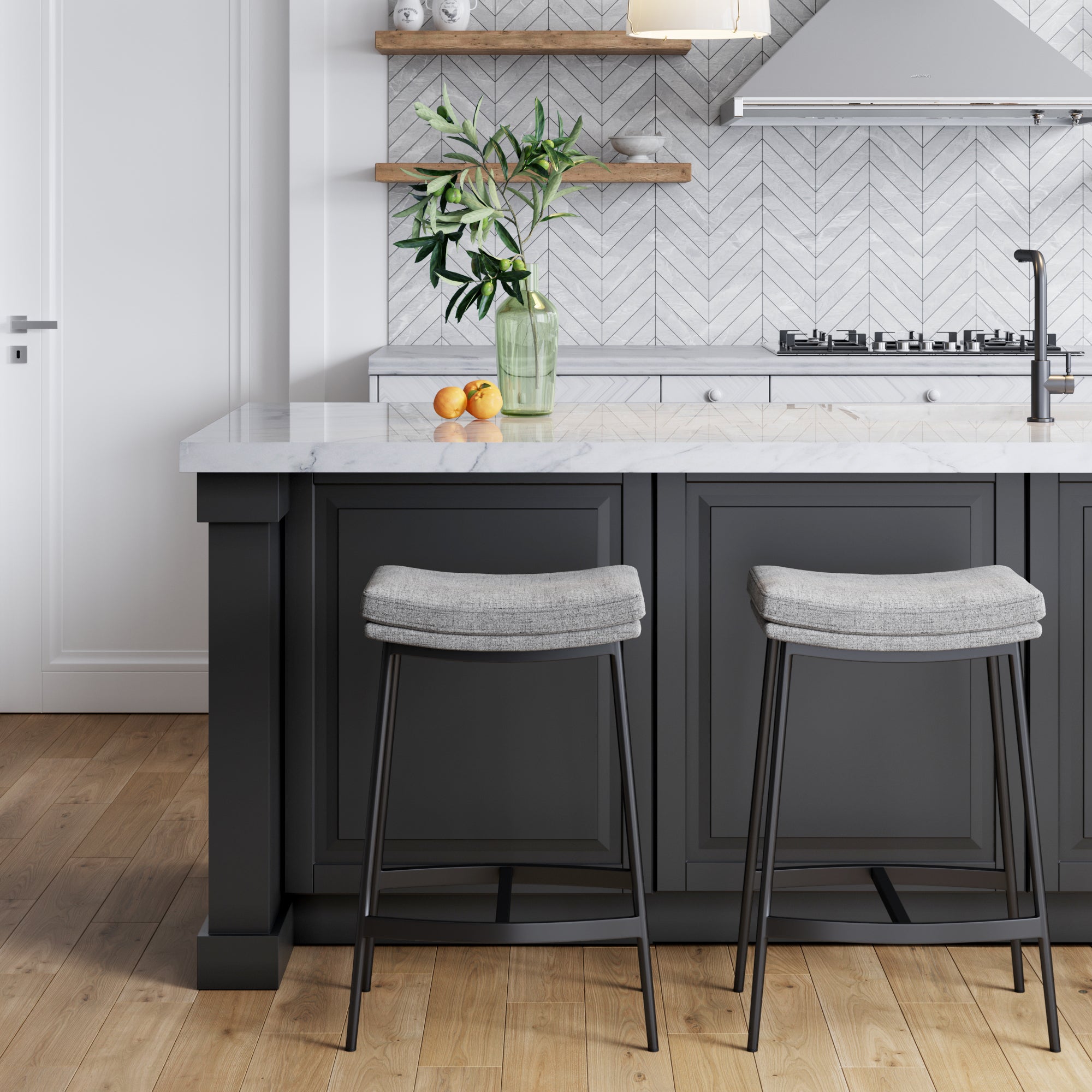 Modern farmhouse kitchen with a dark gray island, two Nathan James Upholstered Counter Height Saddle Bar Stools in gray, wooden floor, marble countertop, leafy branch vase, herringbone backsplash, and open wooden shelves.
