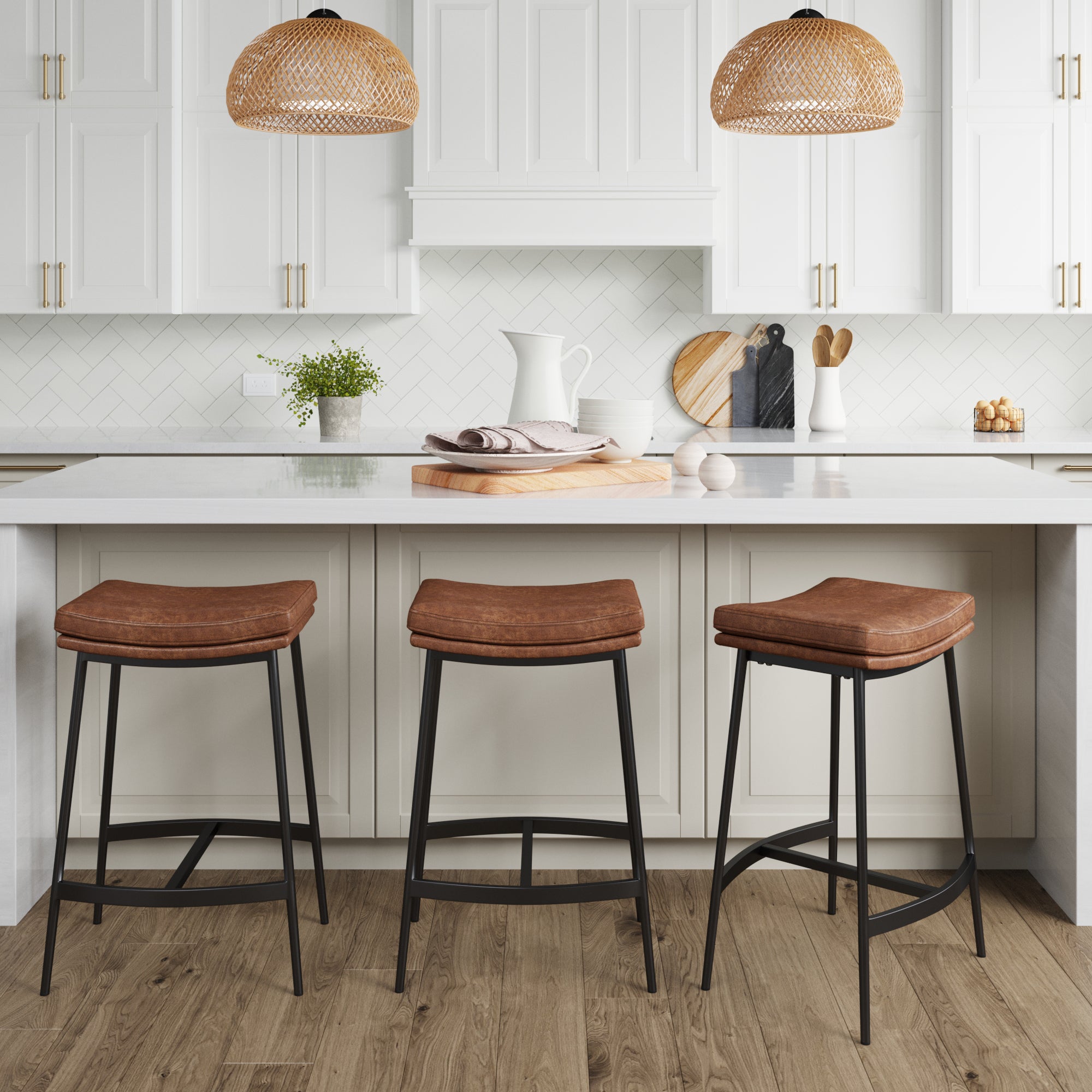 Modern farmhouse kitchen with white cabinets, a white island, and three Nathan James Faux Leather Counter Height Saddle Bar Stools. Two wicker pendant lights hang above the island, with accessories and plants for decor.