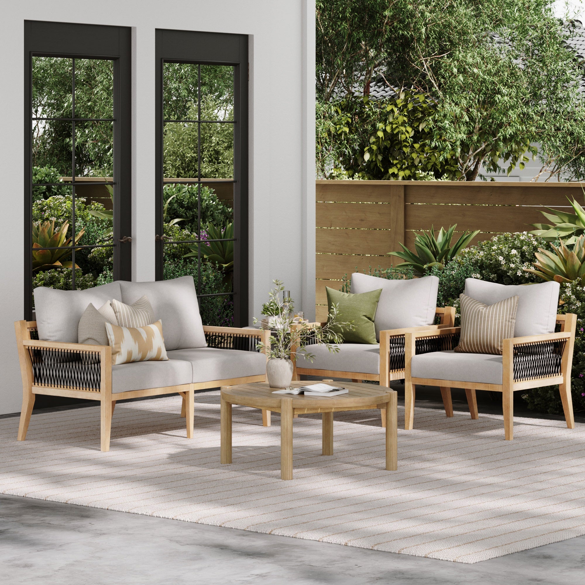 The Nathan James Outdoor 4 Piece Wood Set features a weatherproof acacia wood sofa, two armchairs, and a round patio table for stylish comfort. Cushions and pillows provide coziness, while greenery completes your relaxing outdoor space.