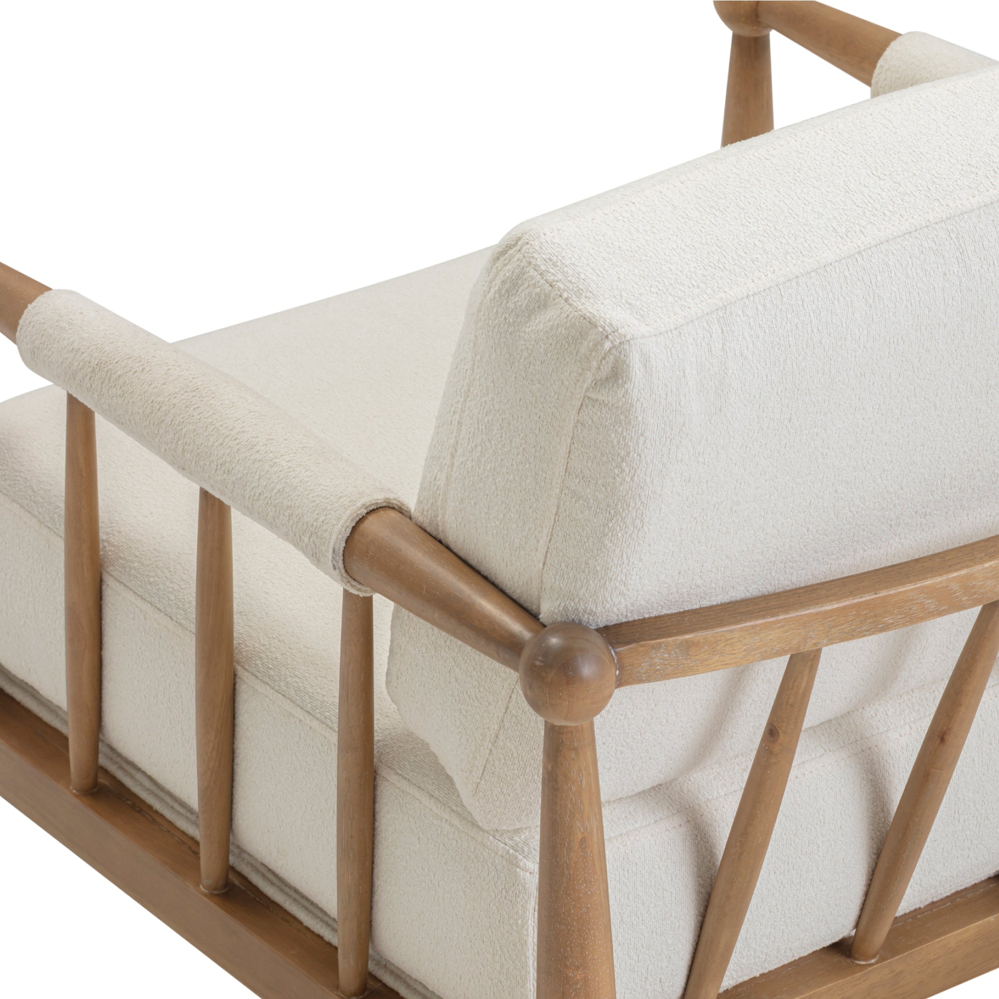 A close-up of a wooden armchair with angled arms, vertical slats, and plush off-white cushions on the seat and backrest. The wood has a natural finish.