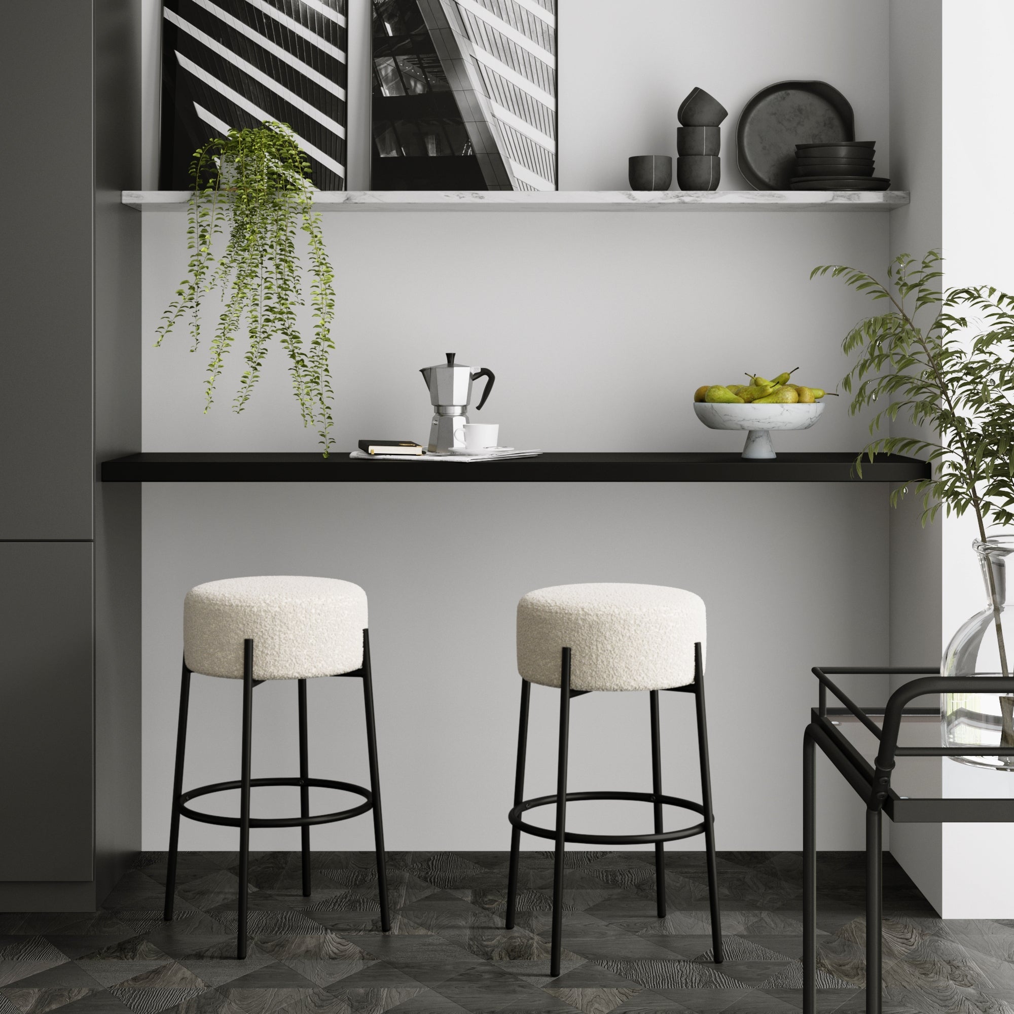 A modern minimalist kitchen features two Nathan James Round Boucle Backless Bar Stools at a black counter, complemented by a hanging plant, coffee maker, fruit bowl, and monochrome architecture photos for a sleek look.