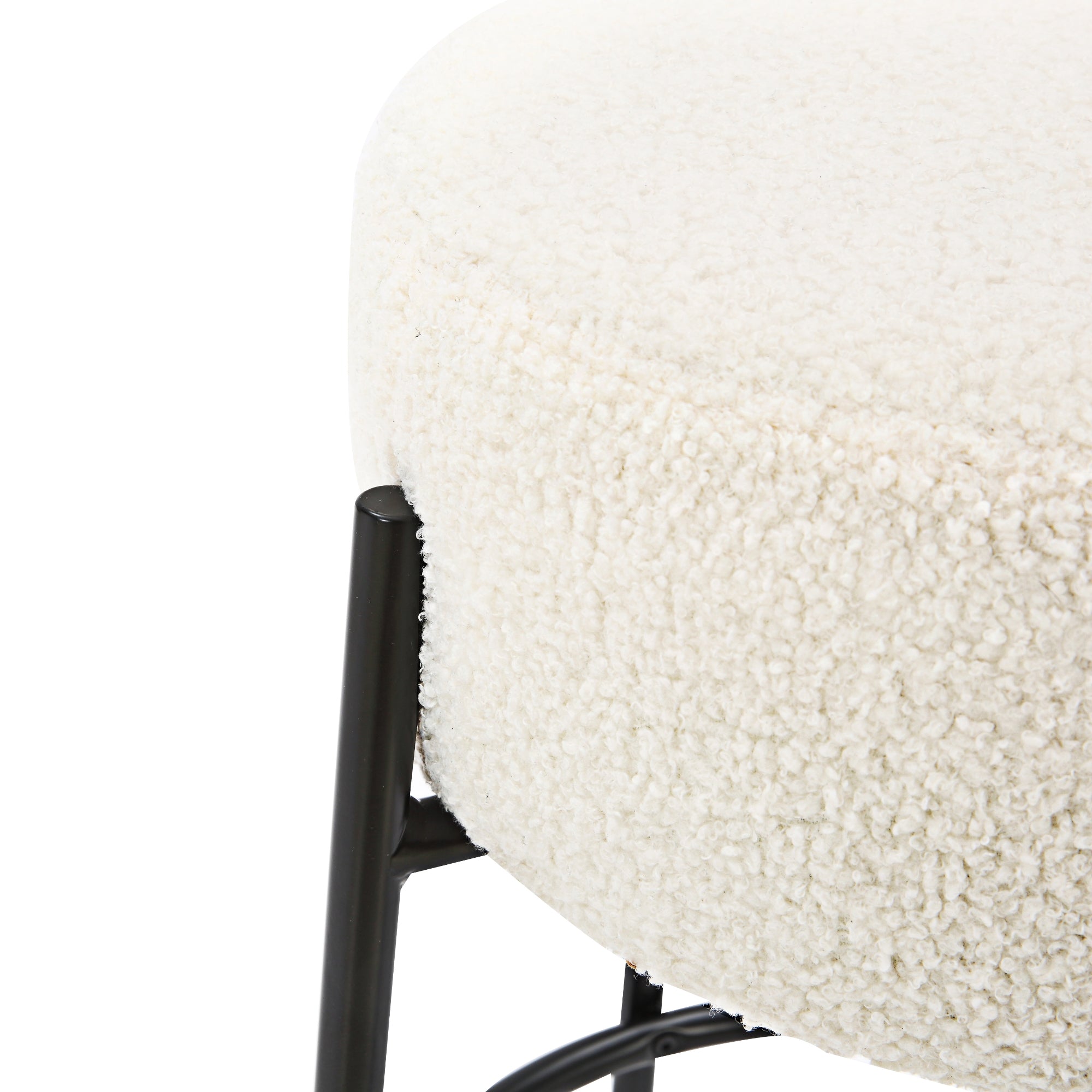 Close-up of a round, cushioned stool with a soft, cream-colored, textured fabric and black metal legs.