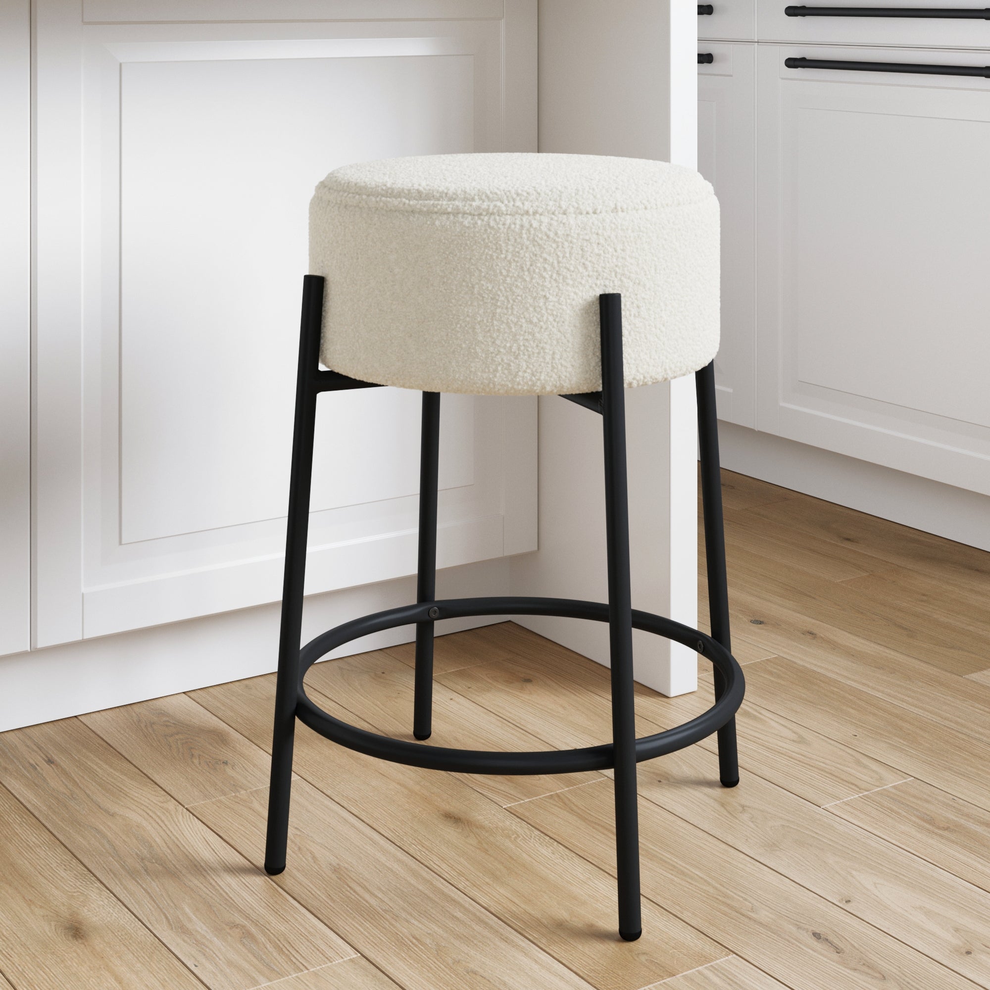 A modern kitchen features a round, white cushioned stool with black metal legs and a circular footrest, placed on light wood flooring near white cabinets.