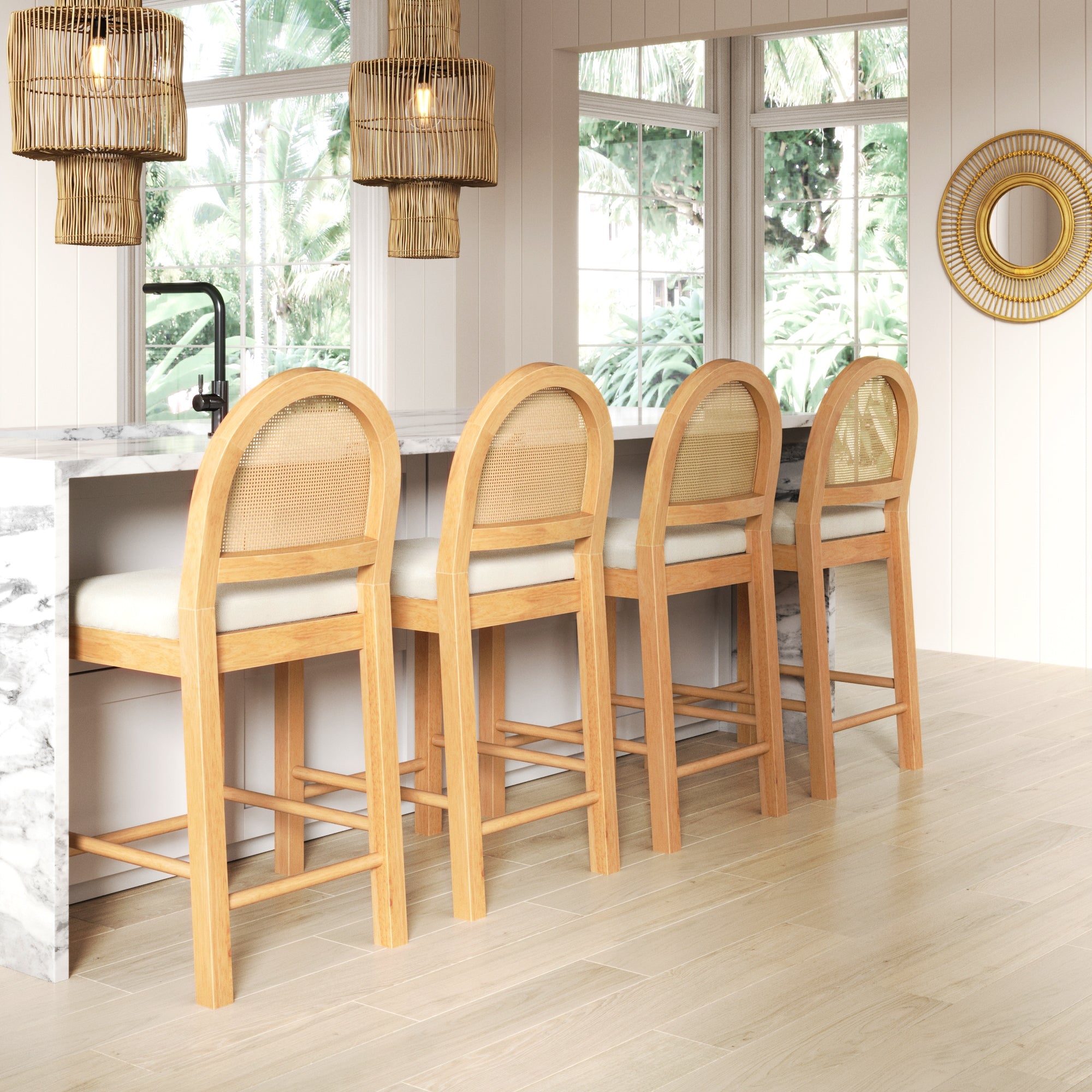 Four wooden barstools with woven backs and cream cushions are lined up at a marble kitchen island. Pendant lights and large windows with a view of greenery brighten the modern, airy space.