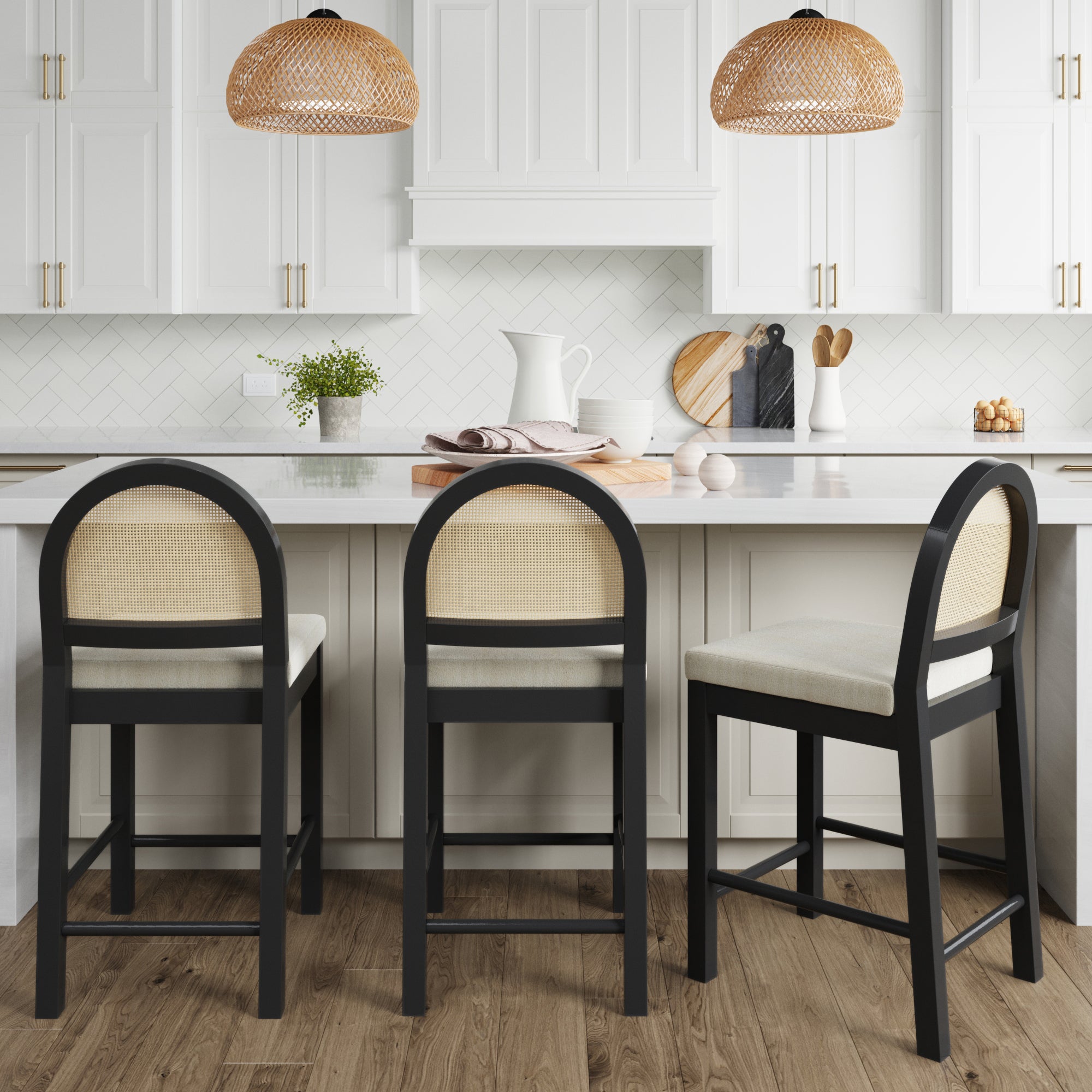 Three Boucle & Rattan Counter Height Bar Stools Black (Set of 3) by Nathan James, featuring woven rattan backrests and black frames, are placed at a white kitchen island in a bright, minimalist space with white cabinetry and pendant lights.