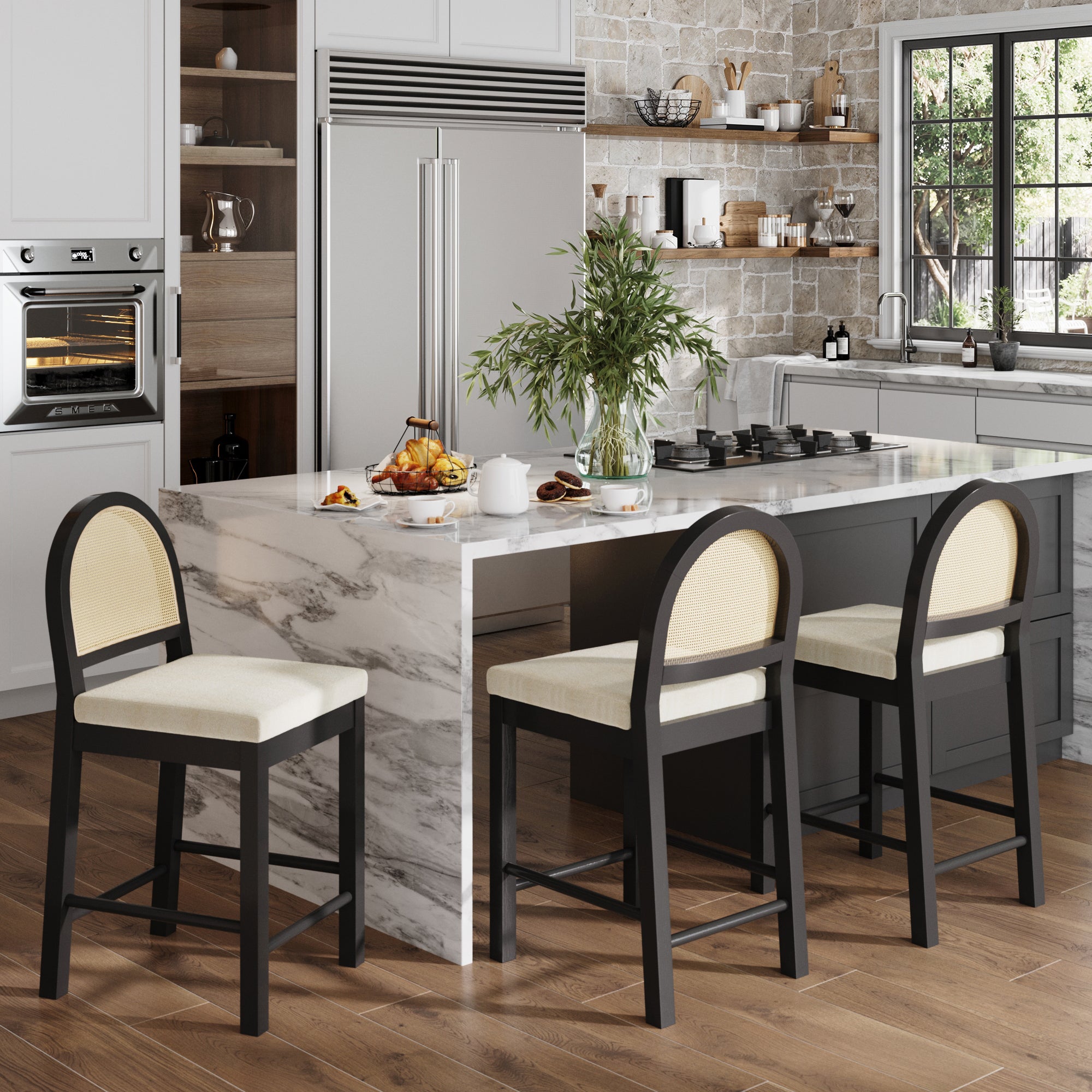 Modern kitchen with a marble island, Nathan James Boucle & Rattan Counter Height Bar Stools Black (Set of 3), a vase of greenery, pastries, and kitchenware on the counter. Light wood floors, stone backsplash, and a large window.