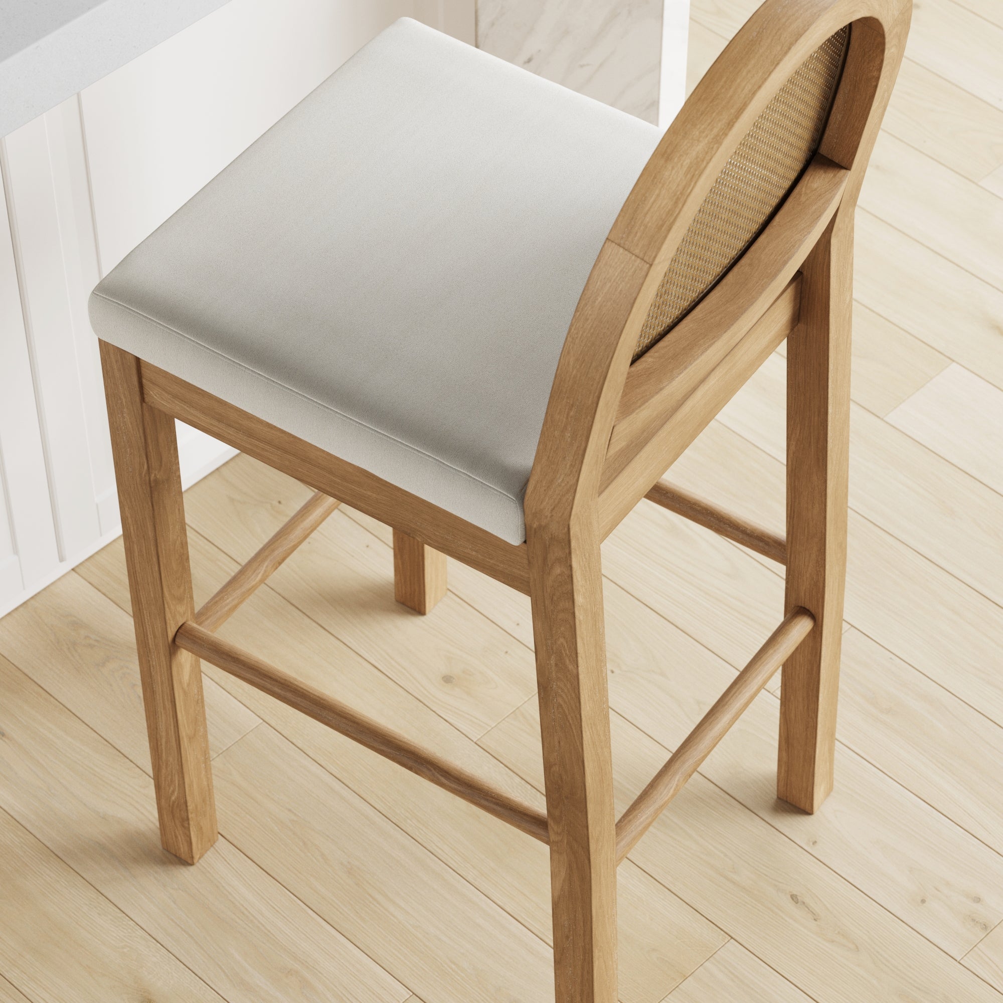 A light wooden bar stool with a cushioned white seat and a rounded backrest, positioned on a light wood floor next to a white counter.