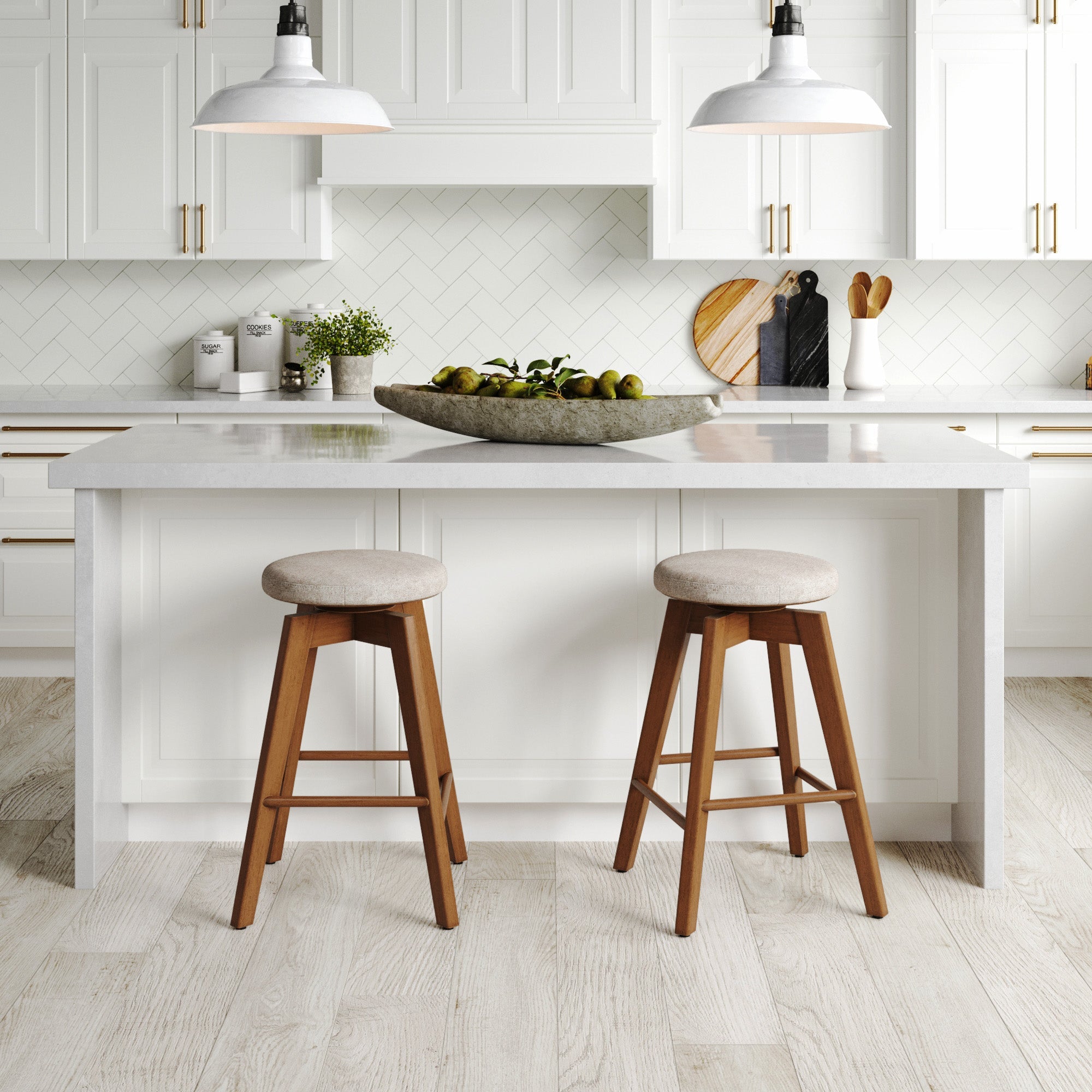 Modern kitchen with white cabinets, marble countertops, and two Nathan James Wood Swivel Counter Height Bar Stools in brown at the island, pendant lights overhead, and a decorative bowl of green fruit as a centerpiece.