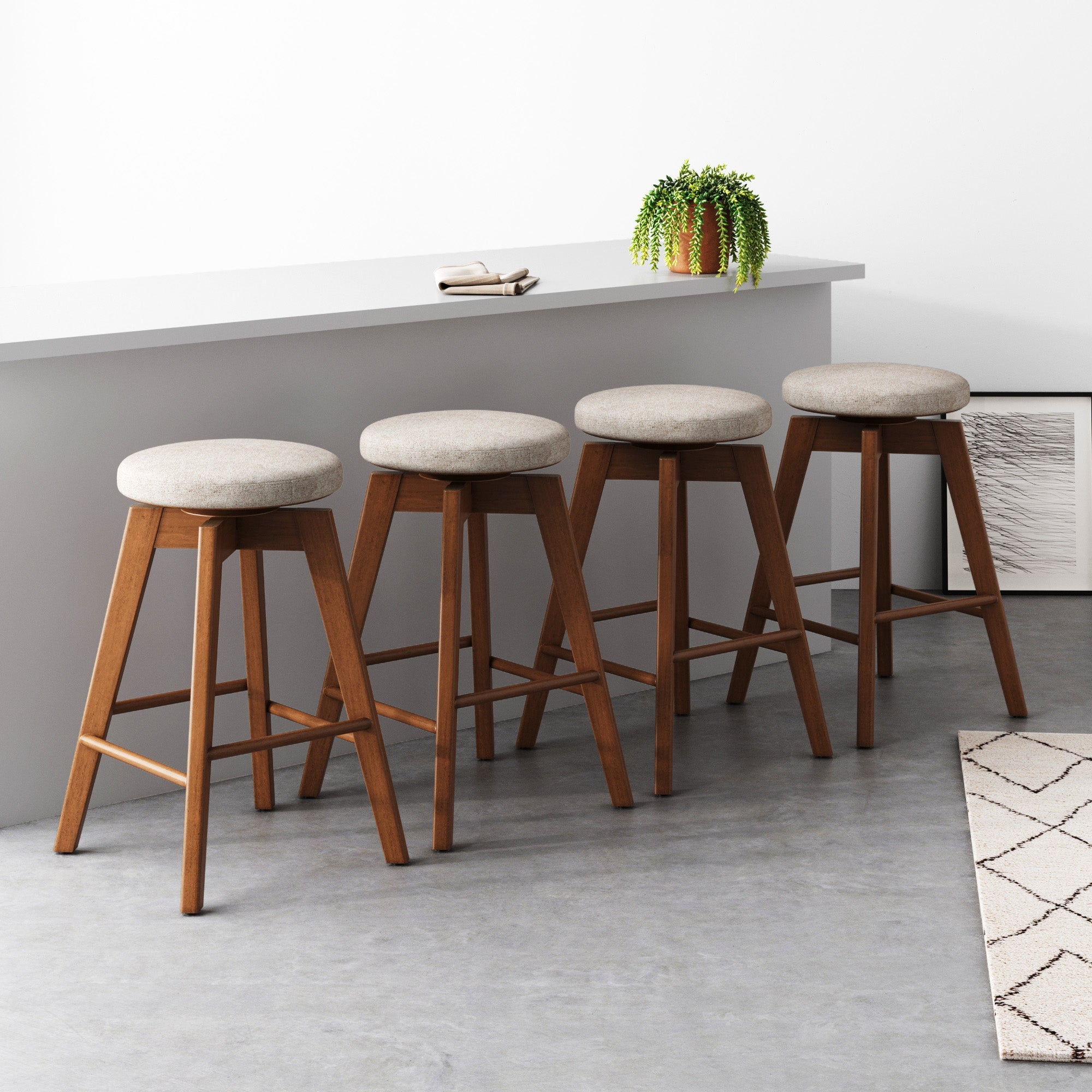 The Nathan James Wood Swivel Counter Height Bar Stools in brown (set of 4) feature round, light gray cushioned seats and line a white counter. A potted plant, books, and art accent the minimalist room—ideal as kitchen island stools.