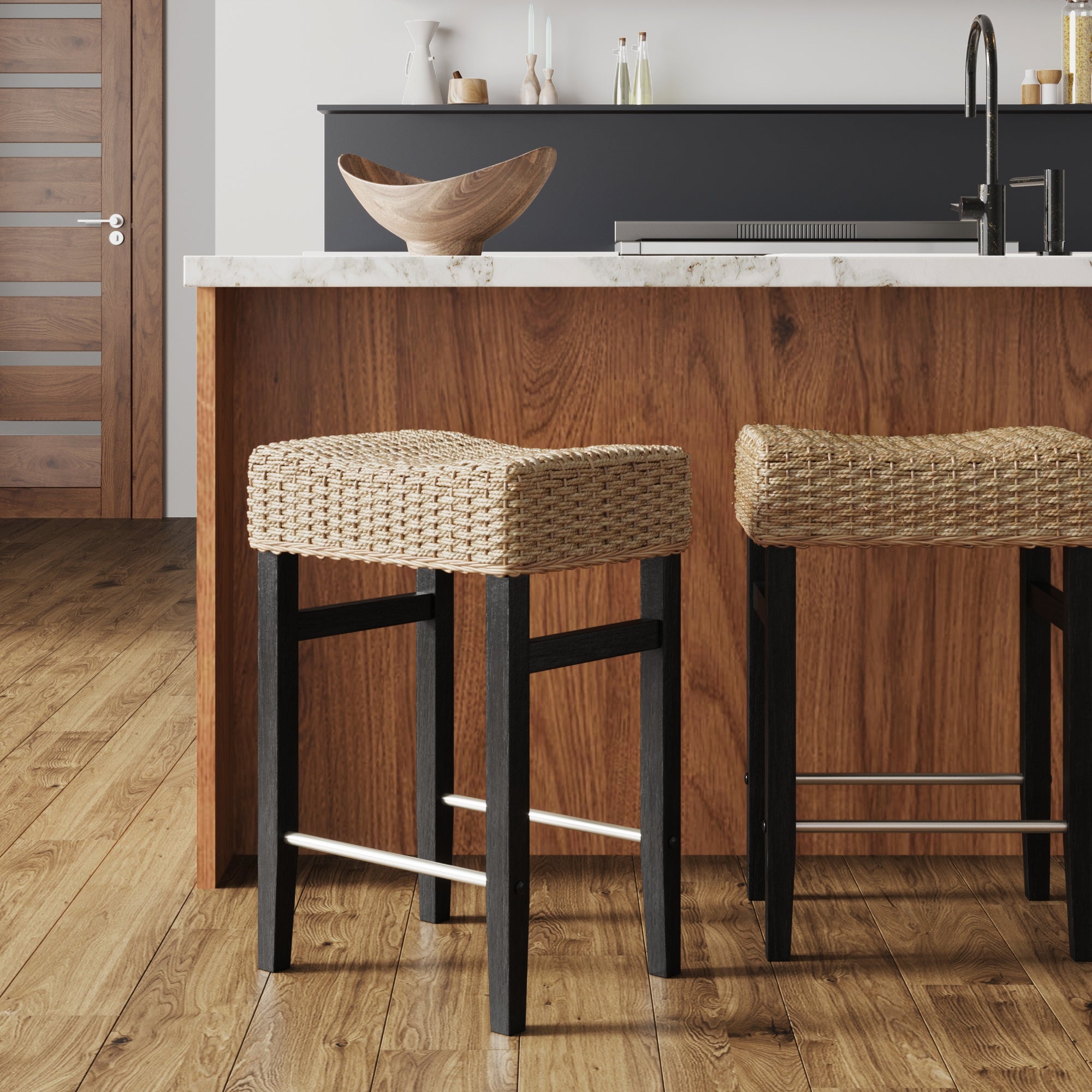 Two woven rattan barstools with dark wood legs are placed at a wooden kitchen island with a light marble countertop in a modern kitchen with wood flooring and minimalist decor.