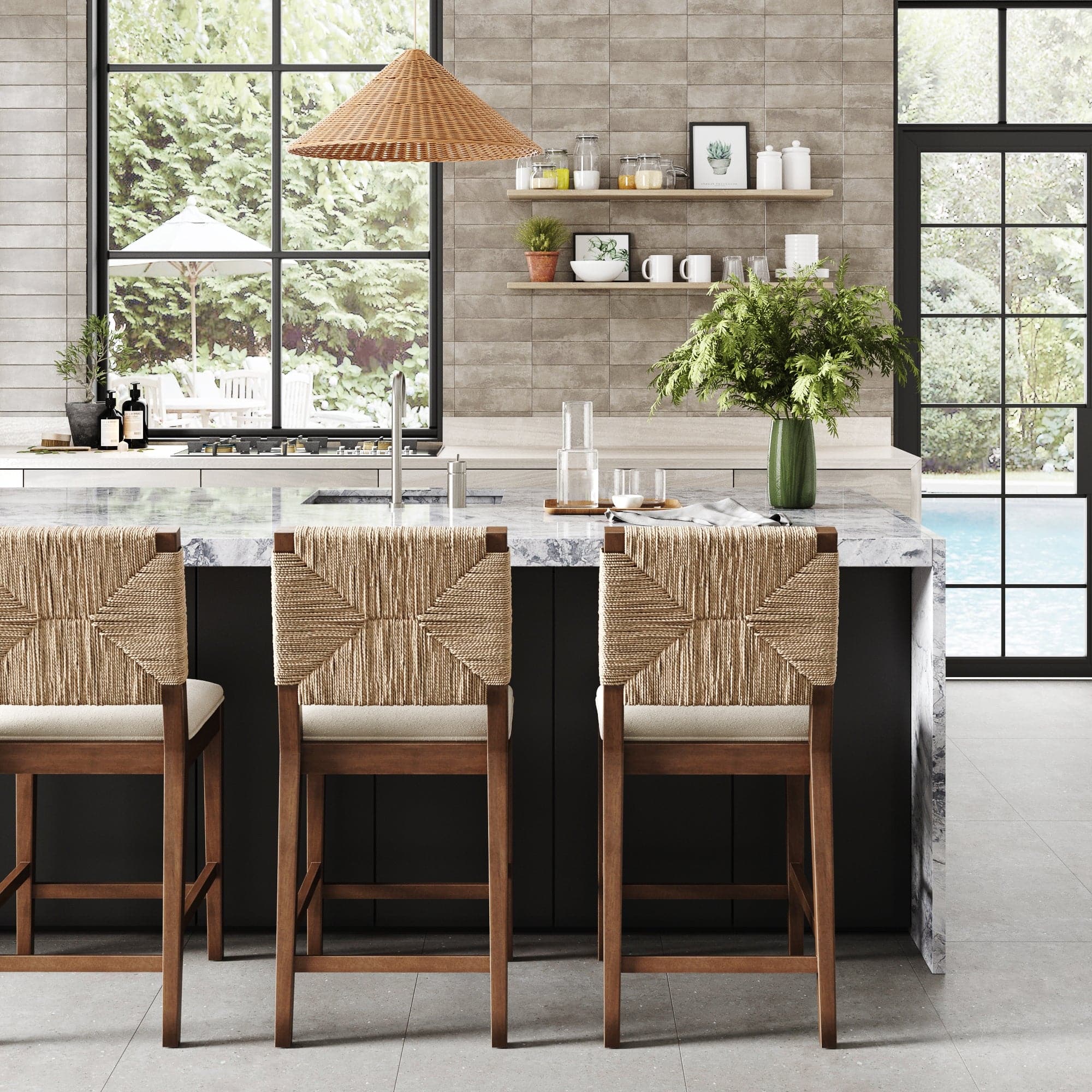 Modern kitchen featuring a marble island, three Nathan James Boucle & Seagrass Counter Height Bar Stools in Dark Brown, a vase of green foliage, open shelves with dishes, large windows, and views of the garden and pool.