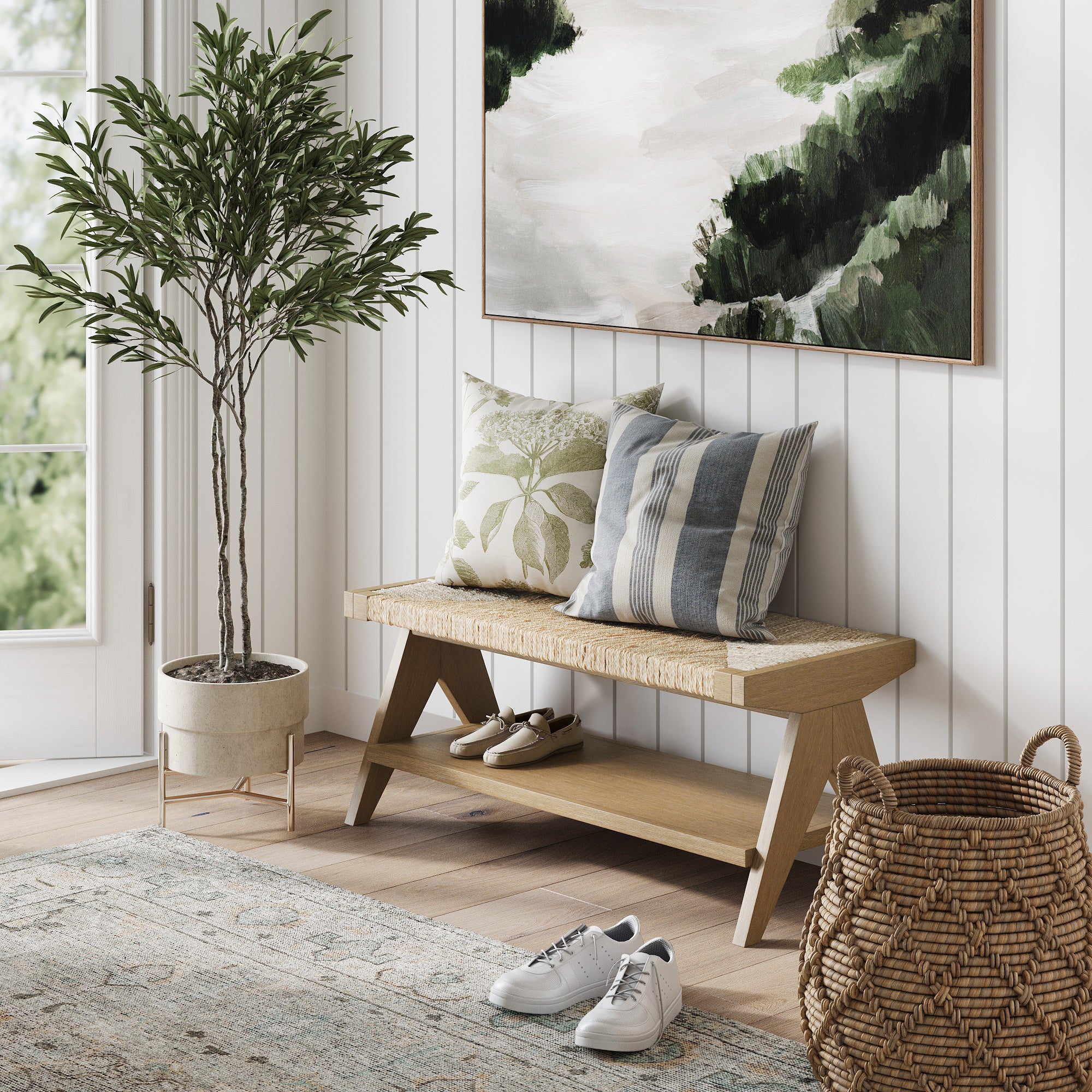 A cozy entryway with a potted plant, a wooden bench with patterned pillows, shoes on the floor and shelf, a woven basket, a rug, and a landscape painting on white paneled walls.
