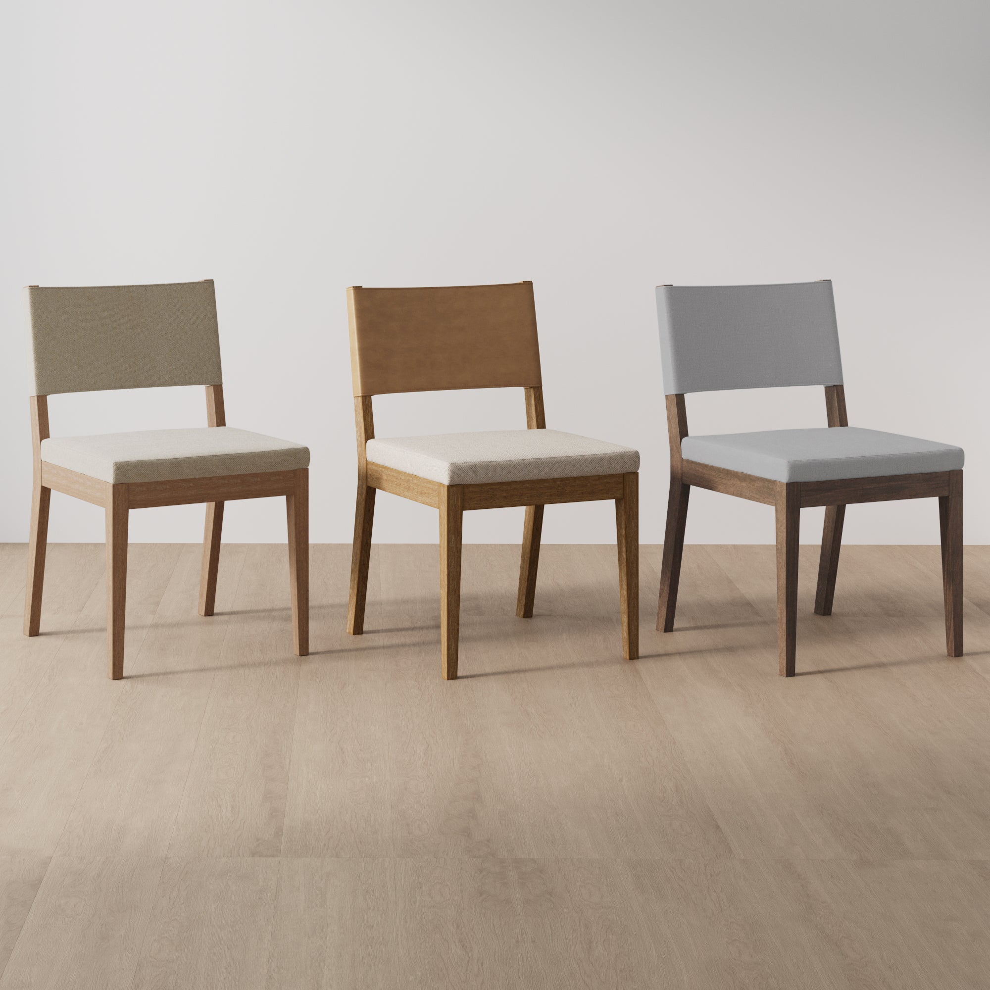 Three wooden chairs with upholstered seats and backs are arranged side by side on a light wood floor; each chair has a different wood finish and fabric color.