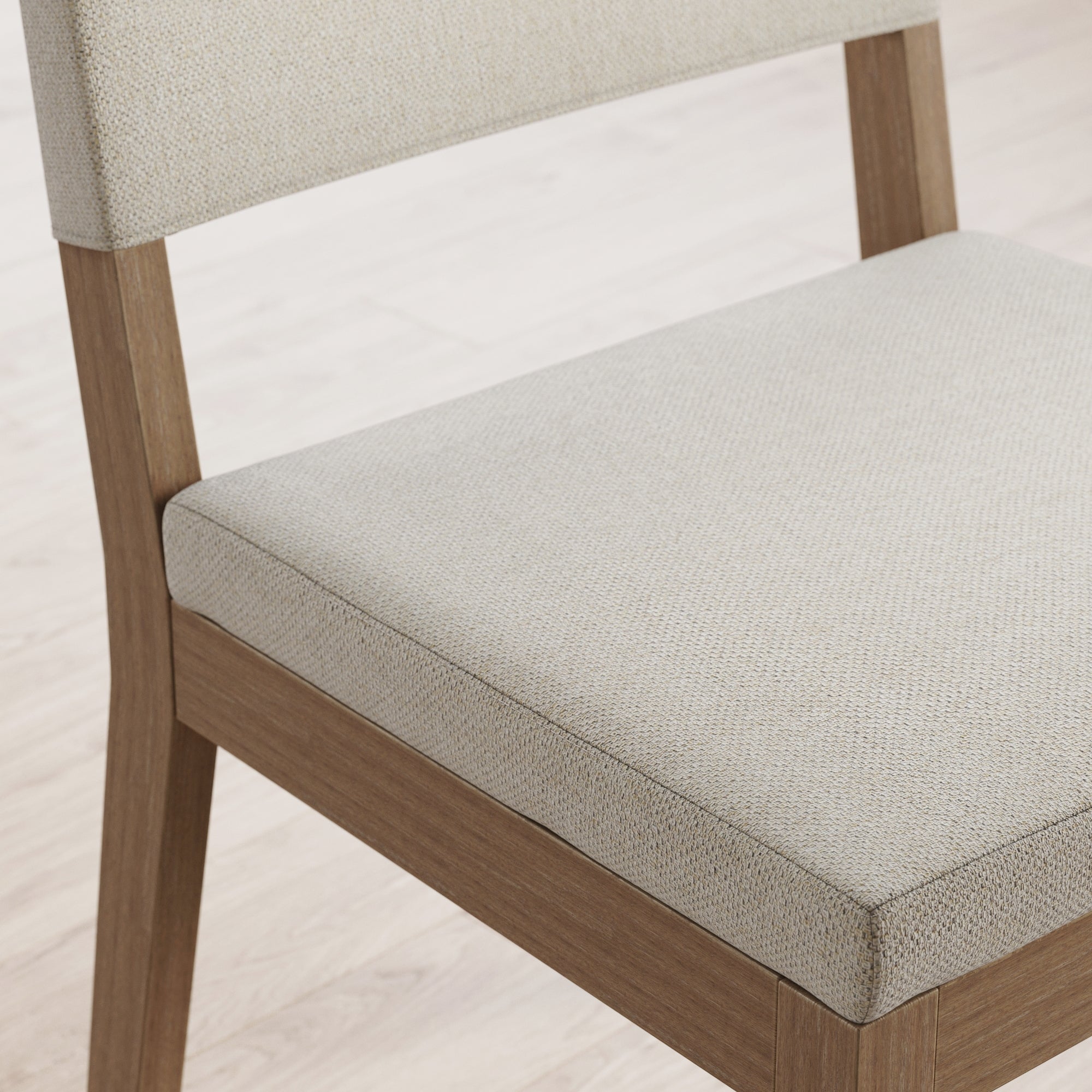 A close-up of a wooden chair with a light beige upholstered seat and backrest, positioned on a light-colored wood floor.