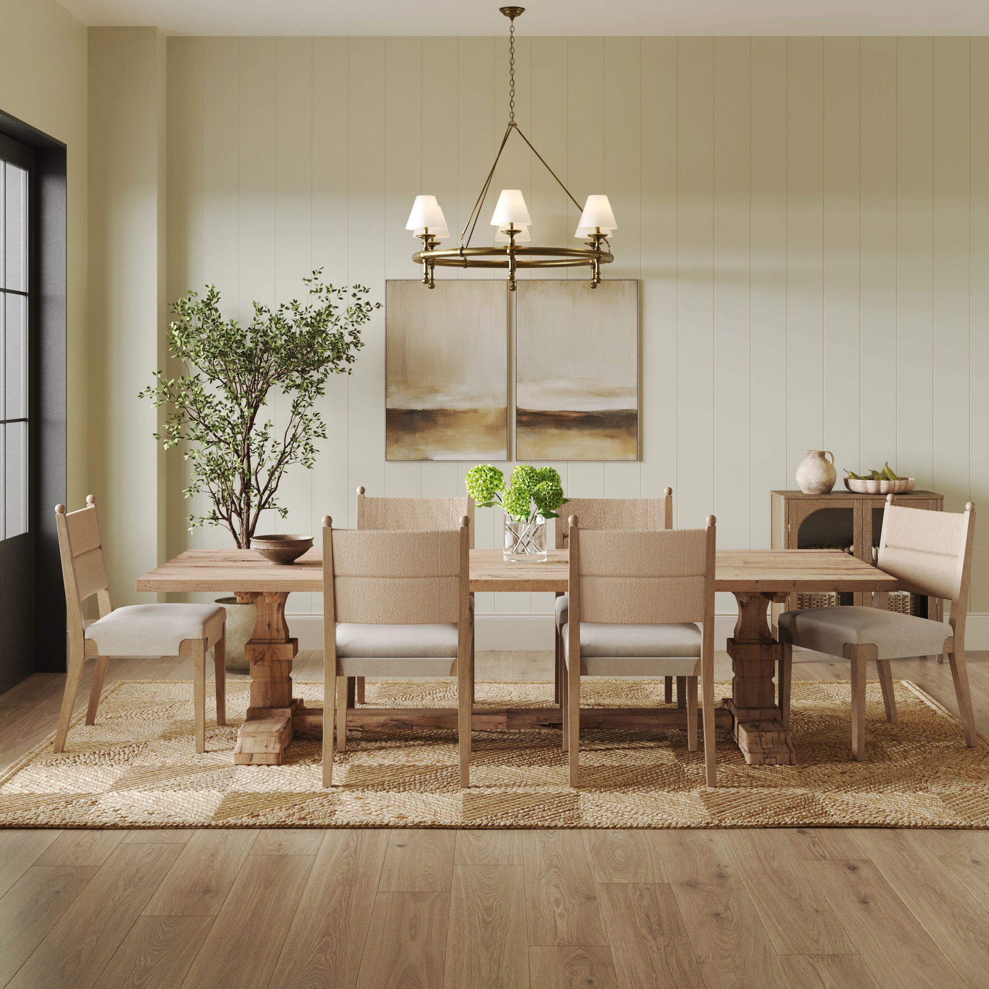 A modern dining room with a wooden table set for six Nathan James Boho Natural Flax & Seagrass Dining Chairs, a chandelier, large potted plant, abstract wall art, and a textured area rug on hardwood flooring.