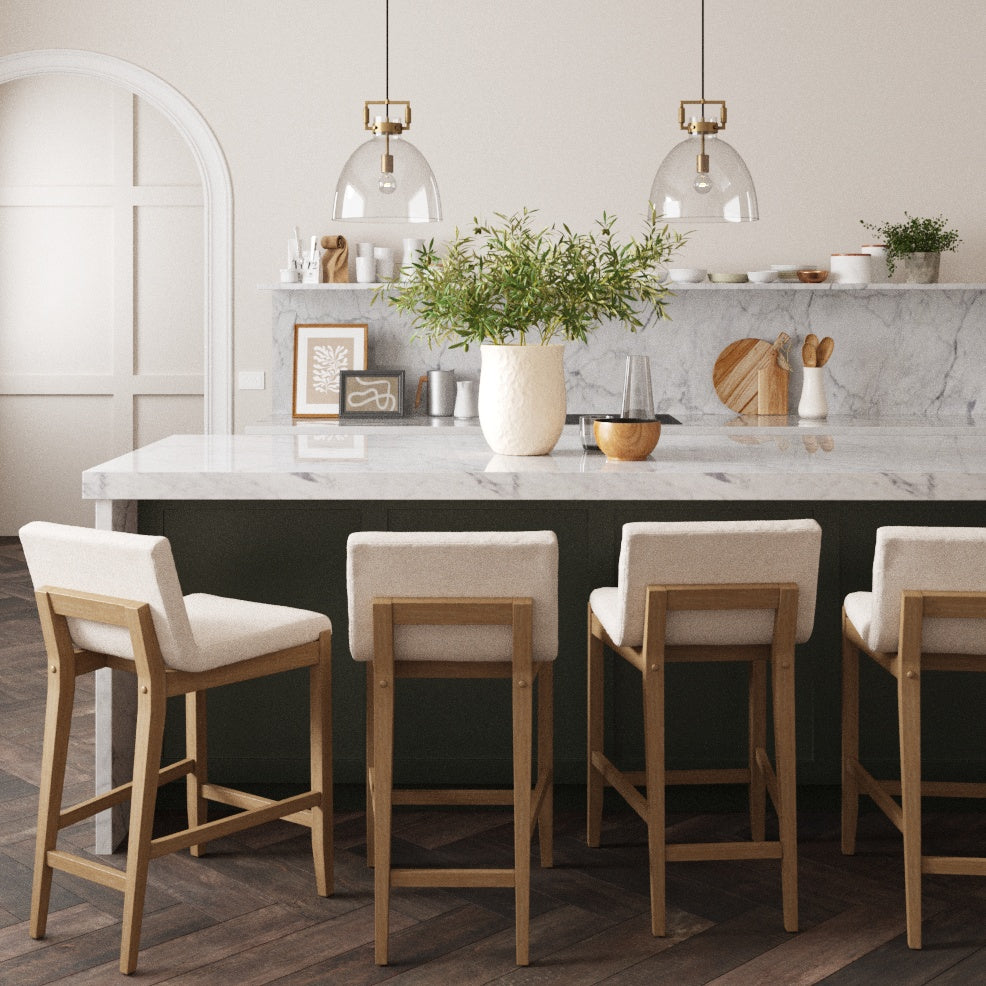 A modern kitchen with a marble island, four wooden barstools with light cushions, pendant lights overhead, and a vase with green branches as a centerpiece, featuring minimalist decor and wooden accents.