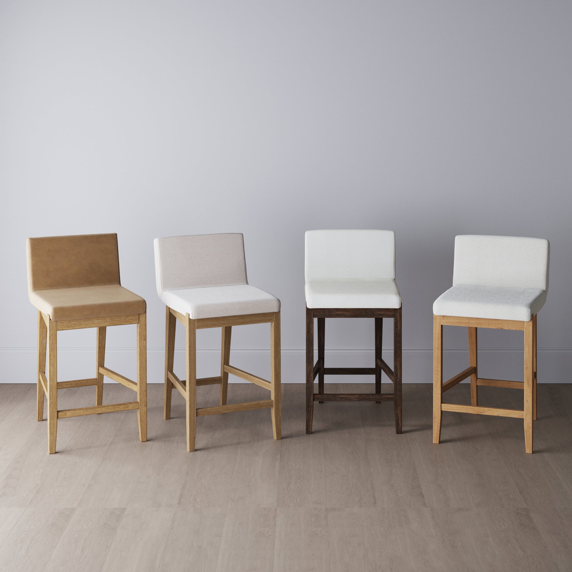 Four modern barstools with backrests are lined up against a light gray wall. Each stool has a different color and wood finish, with upholstered seats and clean, minimalist design. The floor is light wood.