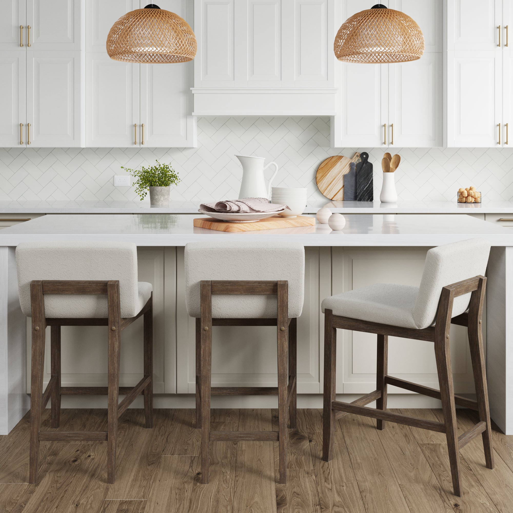 A modern kitchen with a white island, three Nathan James Boucle Counter Height Bar Stools in dark brown, pendant lights with wicker shades, white cabinets, a herringbone backsplash, and decorative accessories on the counter.