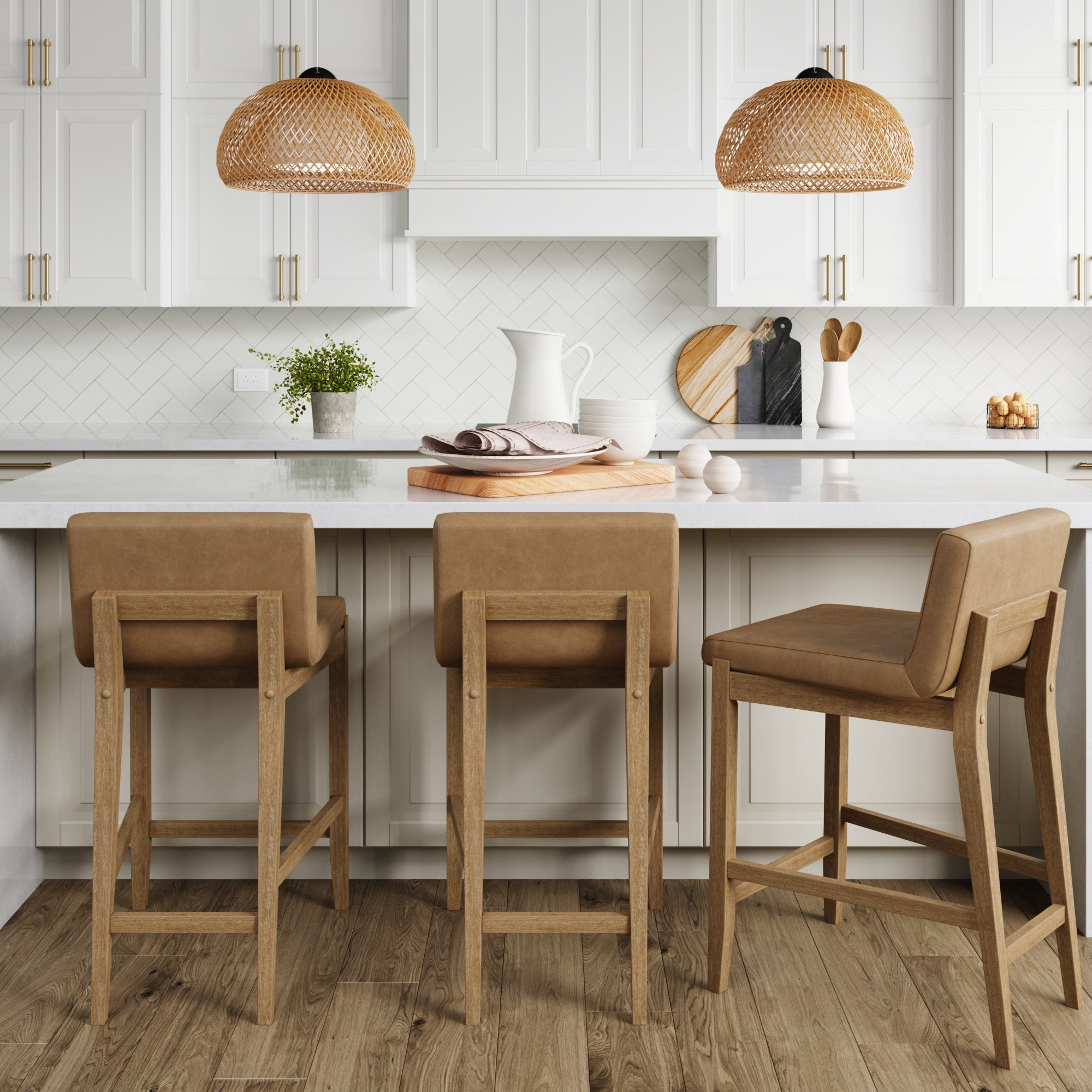 A modern kitchen with white cabinets, a white island countertop, three tan upholstered bar stools, two woven pendant lights, wooden cutting boards, and decorative items on the counter.