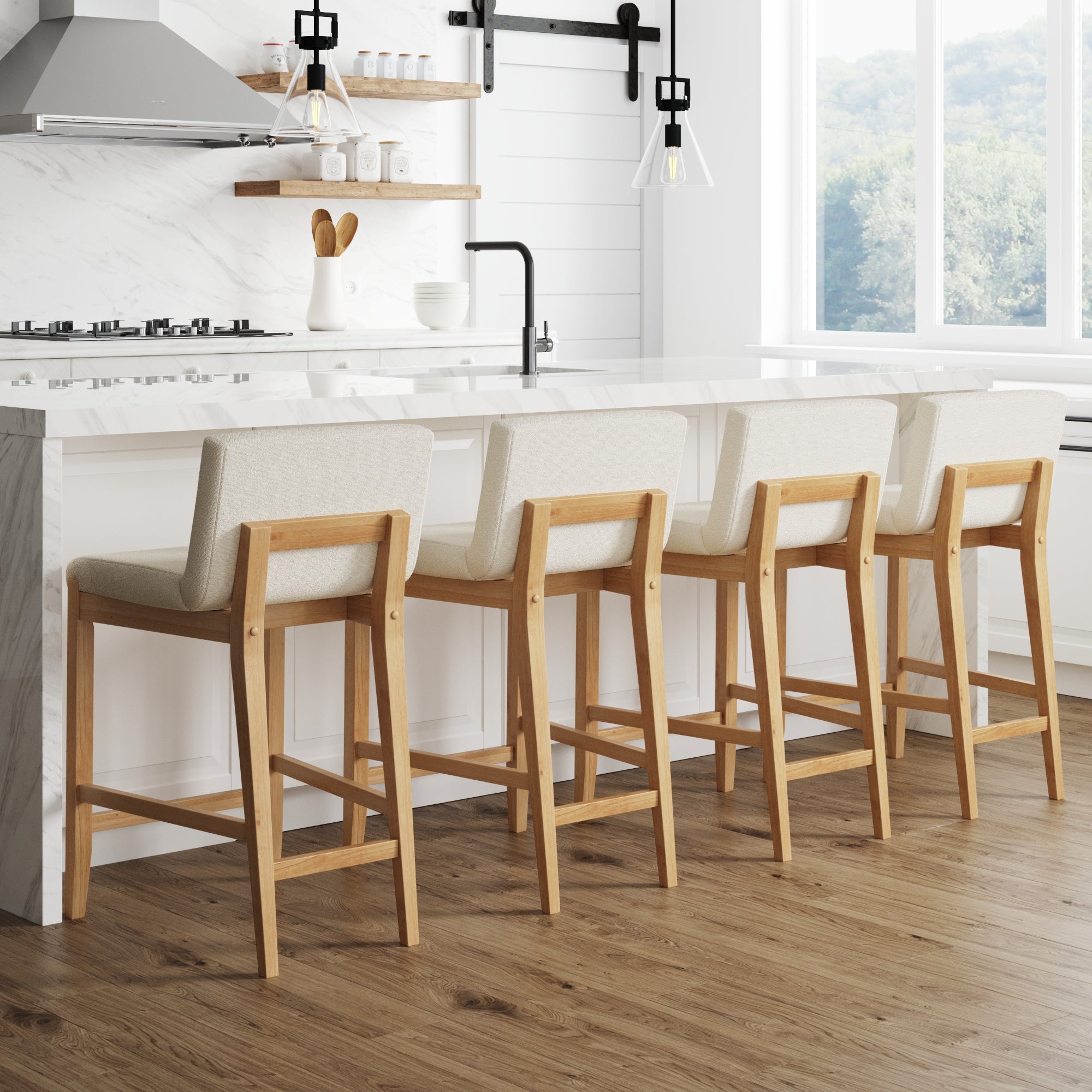 Four wooden bar stools with cream-colored cushions are lined up at a white marble kitchen island in a bright, modern kitchen with large windows, wood flooring, and minimalist decor.