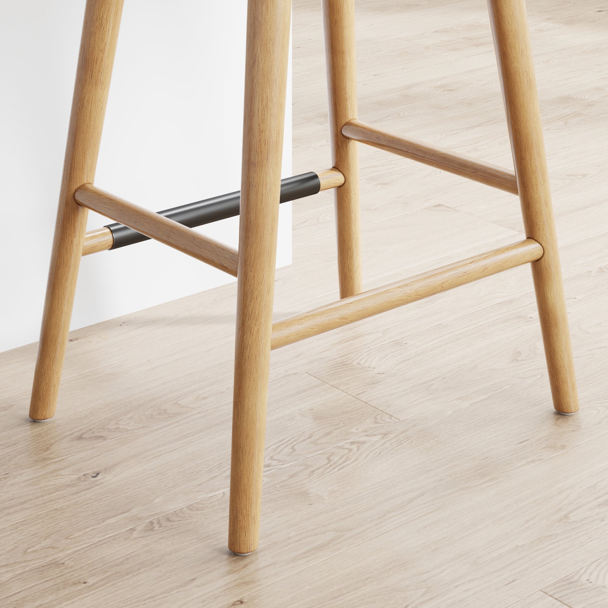Close-up of the legs of a wooden bar stool on a light wood floor, with one of the footrests covered with a black protective sleeve.