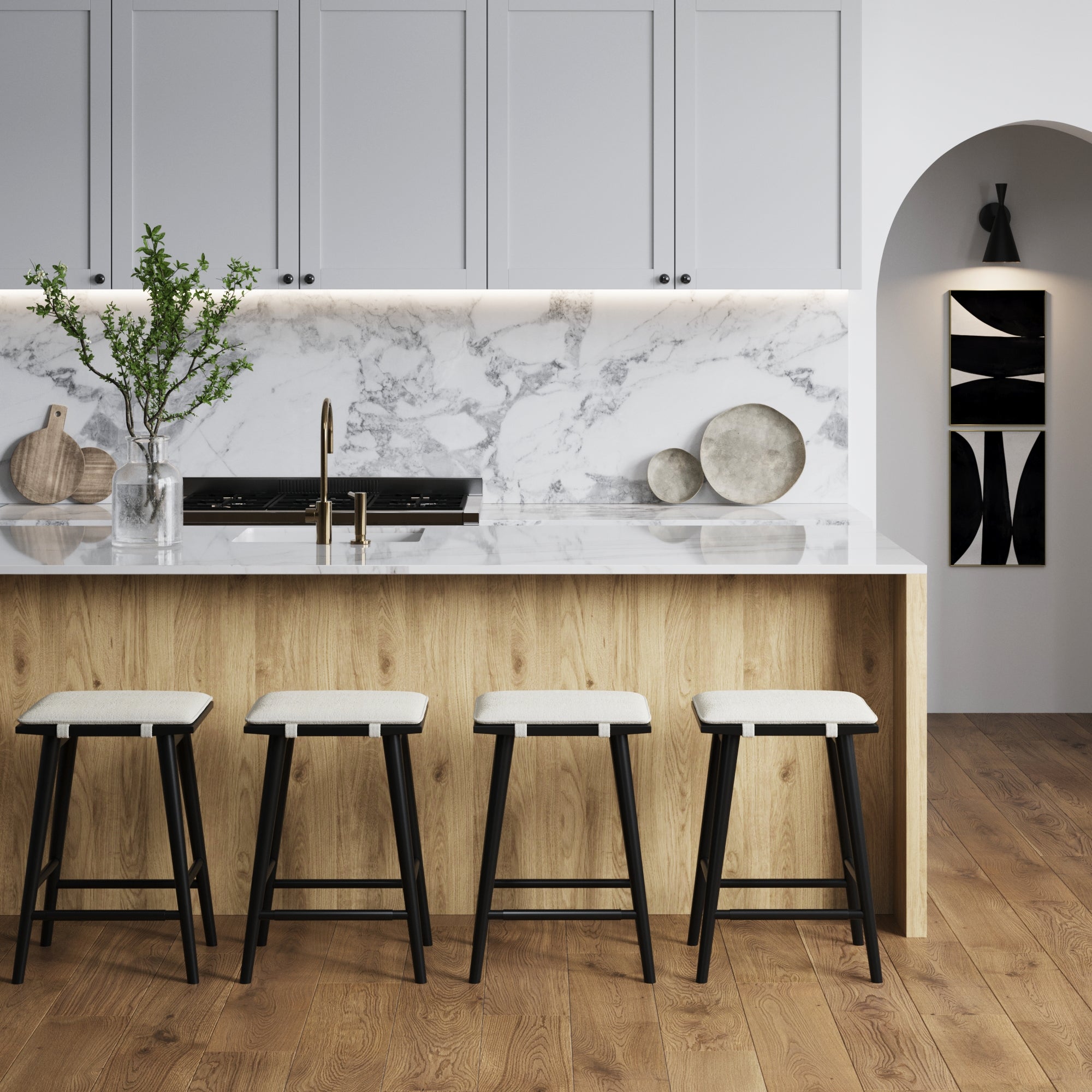 A modern kitchen featuring a wooden island with a white marble countertop and backsplash, four Nathan James Boucle Counter Height Bar Stools (Black), light gray cabinets, brass faucet, wood floors, and minimalist decor.