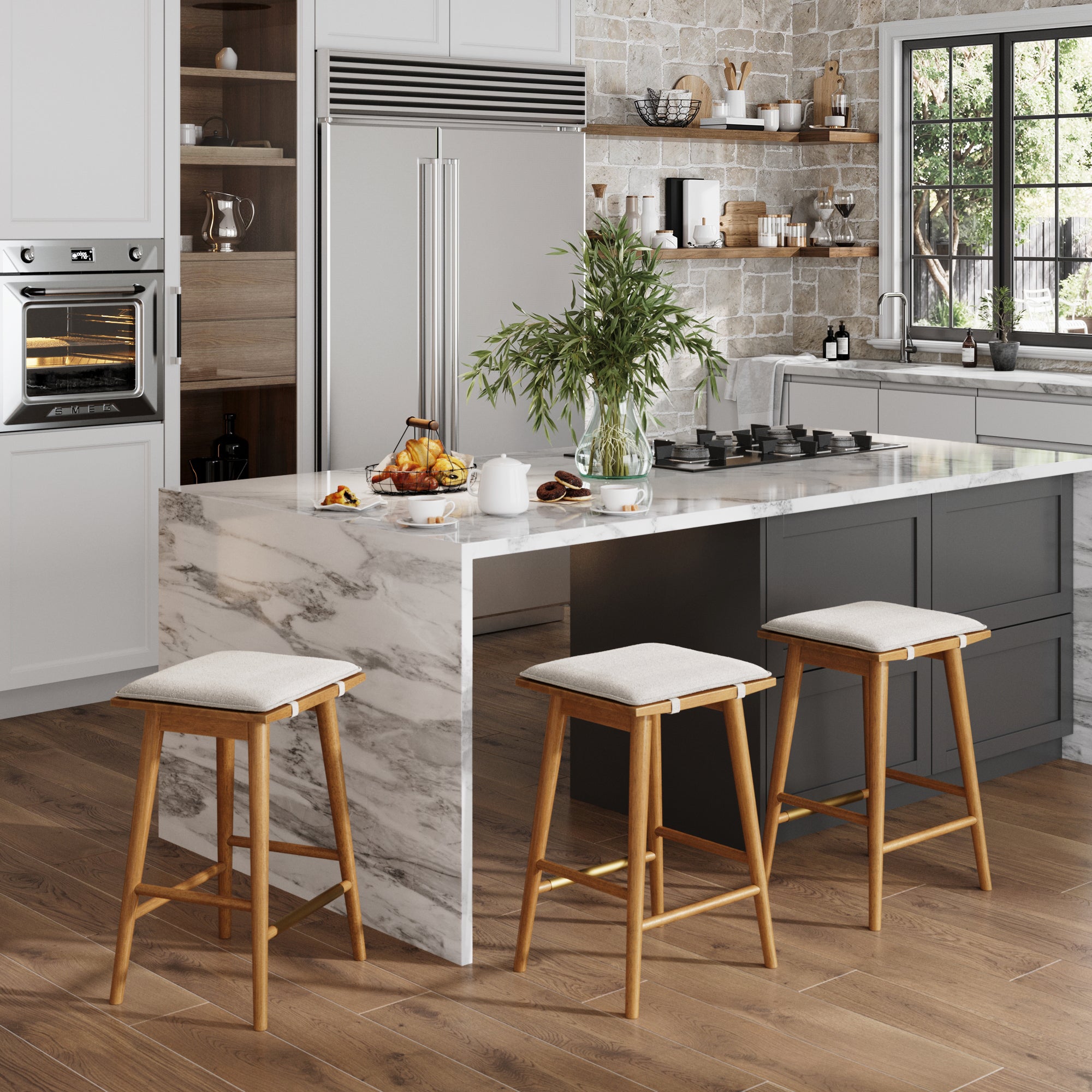 A modern kitchen with a marble island features three Nathan James Boucle Counter Height Bar Stools in brown, a built-in oven, large refrigerator, plant, teapot, cups, and croissants on the island as sunlight streams through the window.