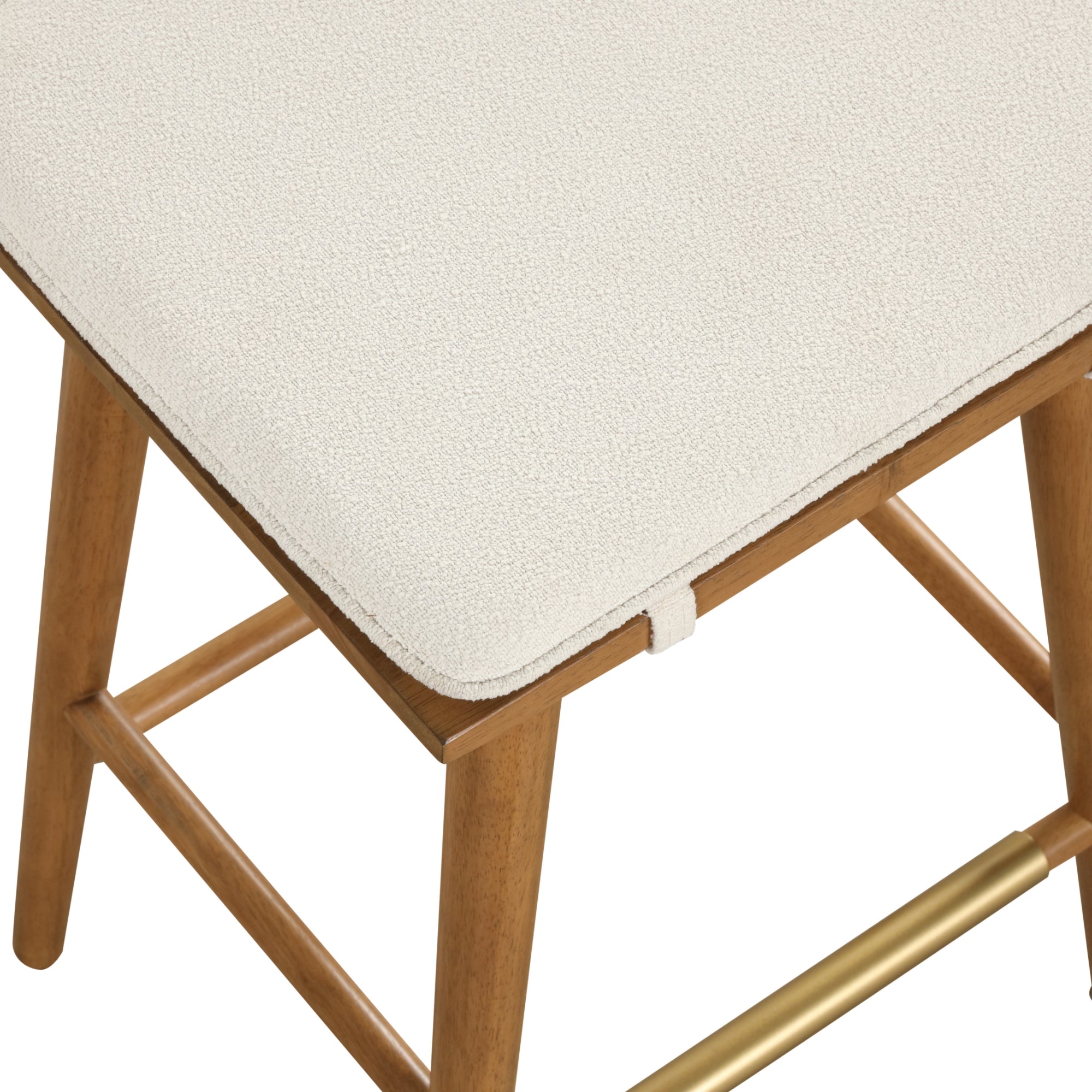A close-up of a wooden stool with a light-colored, textured upholstered seat, featuring angled legs and a horizontal gold bar as a footrest.