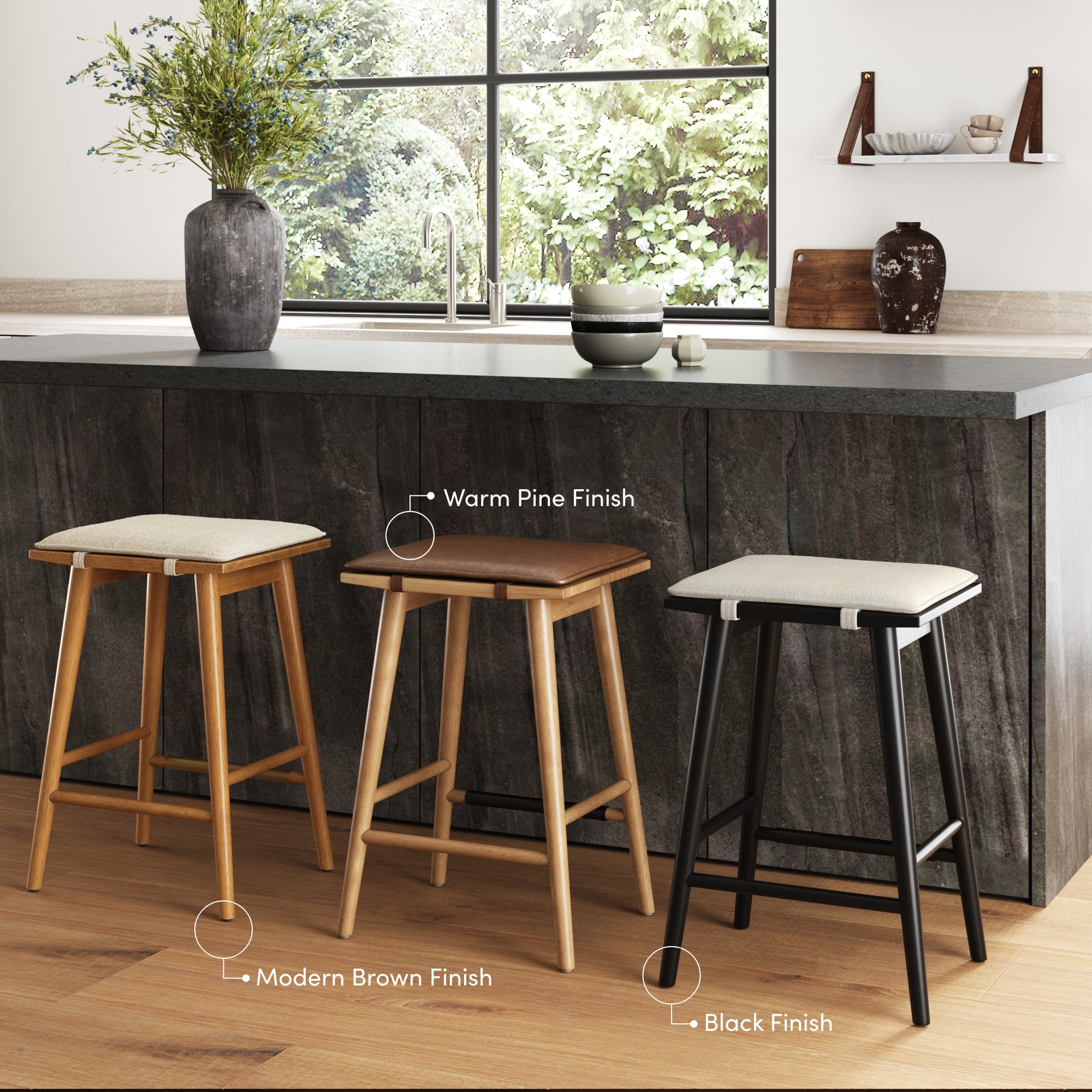 Three bar stools with padded seats are arranged by a kitchen island; the stools have legs in warm pine, modern brown, and black finishes. A large window, sink, and decorative items are in the background.