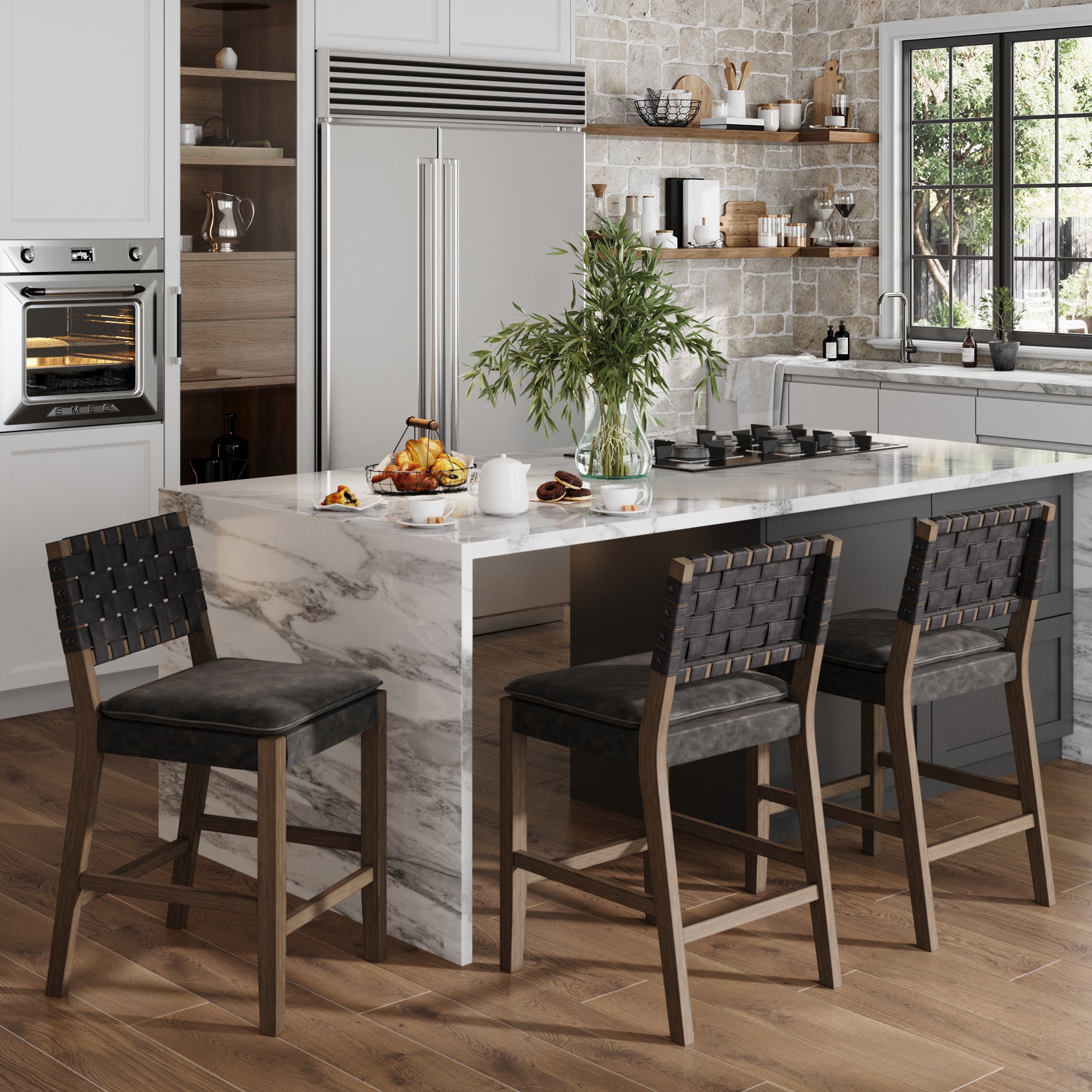 Modern kitchen with a marble island, three Nathan James Faux Leather Woven Counter Height Bar Stools in black, wooden floor, built-in oven, refrigerator, and large window. Island set with breakfast items and a vase of leafy branches.