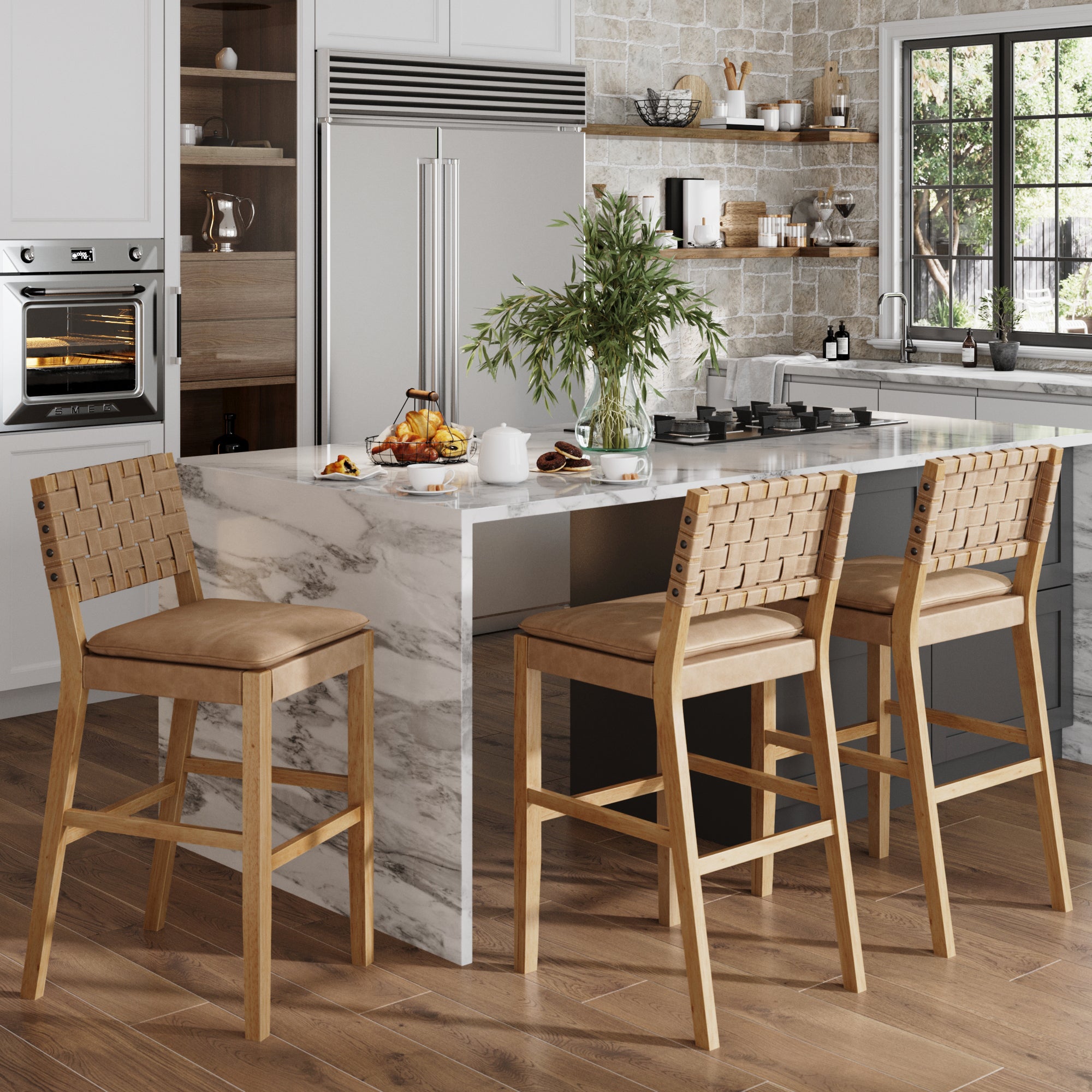 A modern kitchen with a marble island, three Nathan James Faux Leather Woven Bar Stools in brown, a stainless steel refrigerator, built-in oven, plants on the counter, and large windows letting in natural light.